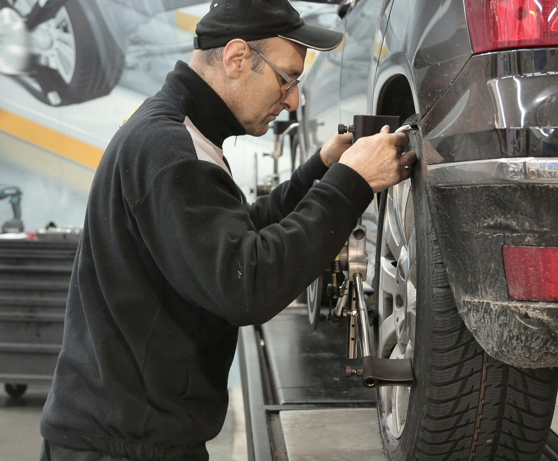 Mechanic aligning car's rear tire on a lift in a shop, using tools.