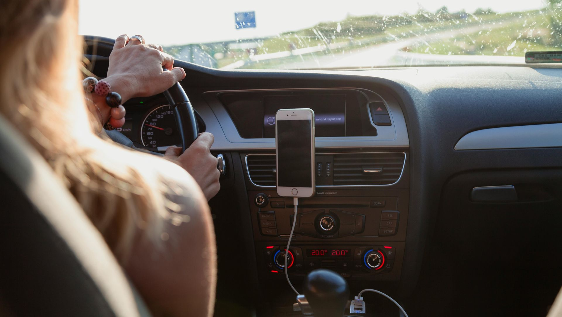 Person driving a car, hands on the steering wheel, smartphone mounted on the dashboard.
