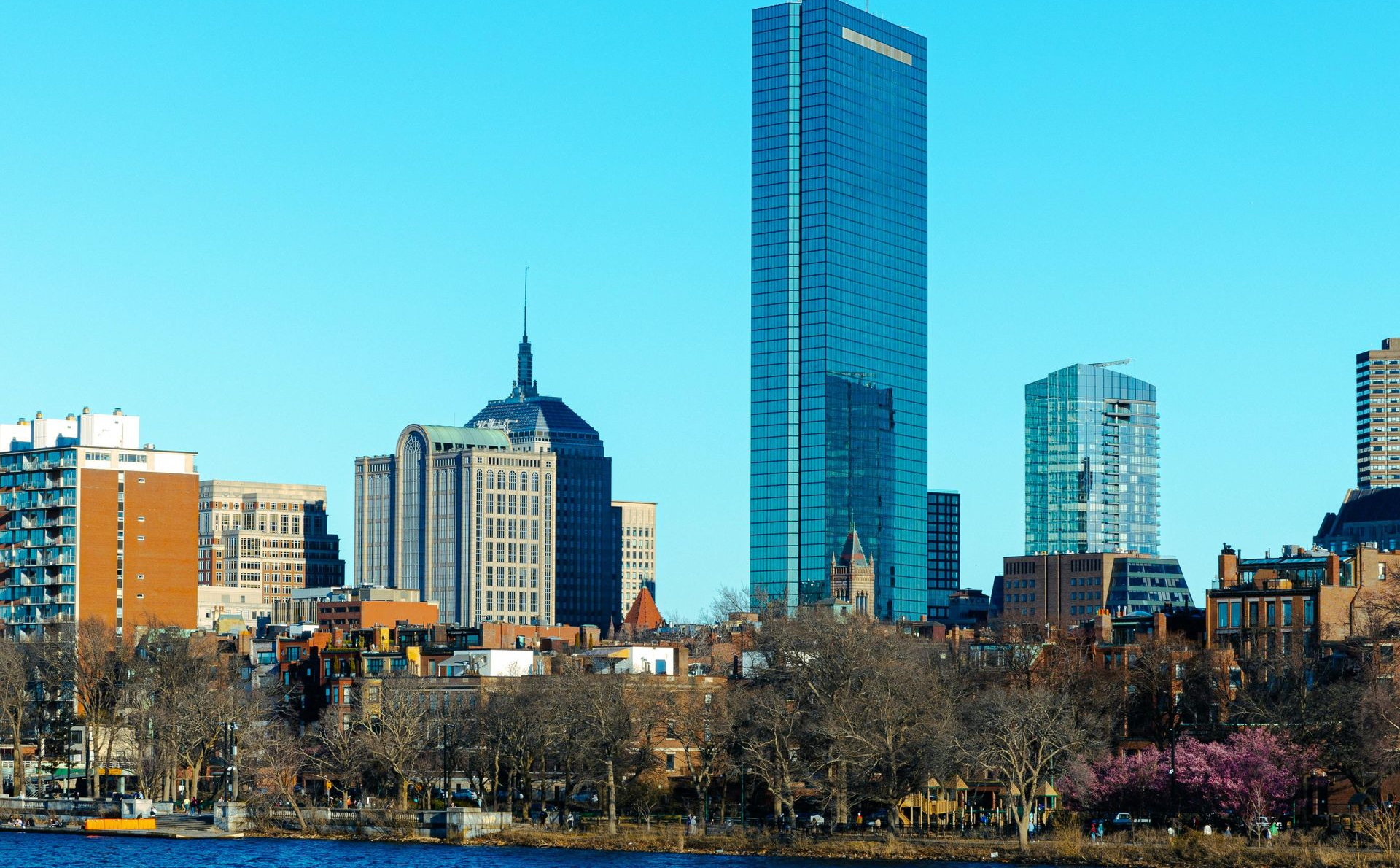 Boston skyline with tall blue glass skyscraper, and other buildings against blue sky.