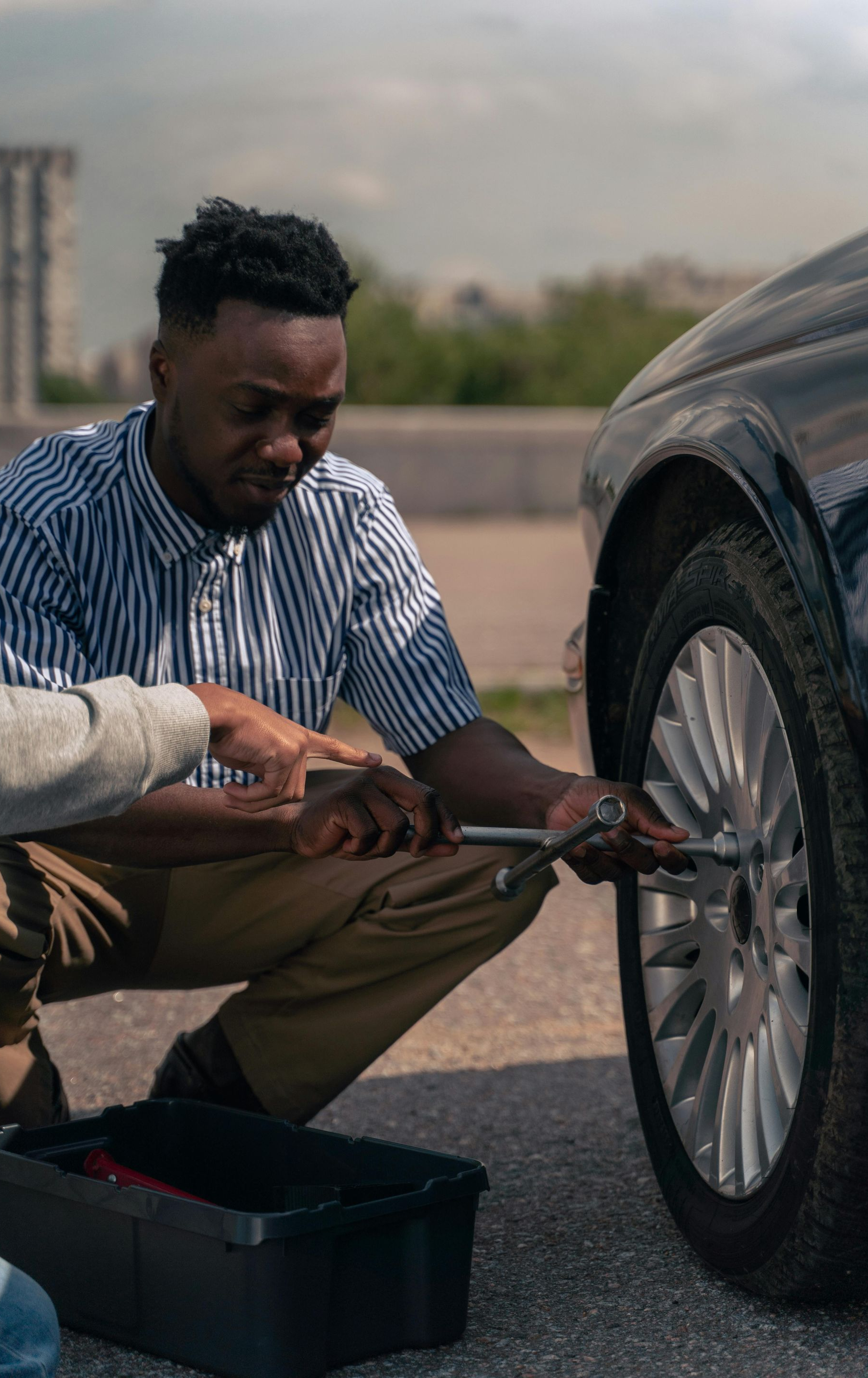 Man crouches next to a car, using a wrench. A toolbox is on the ground.