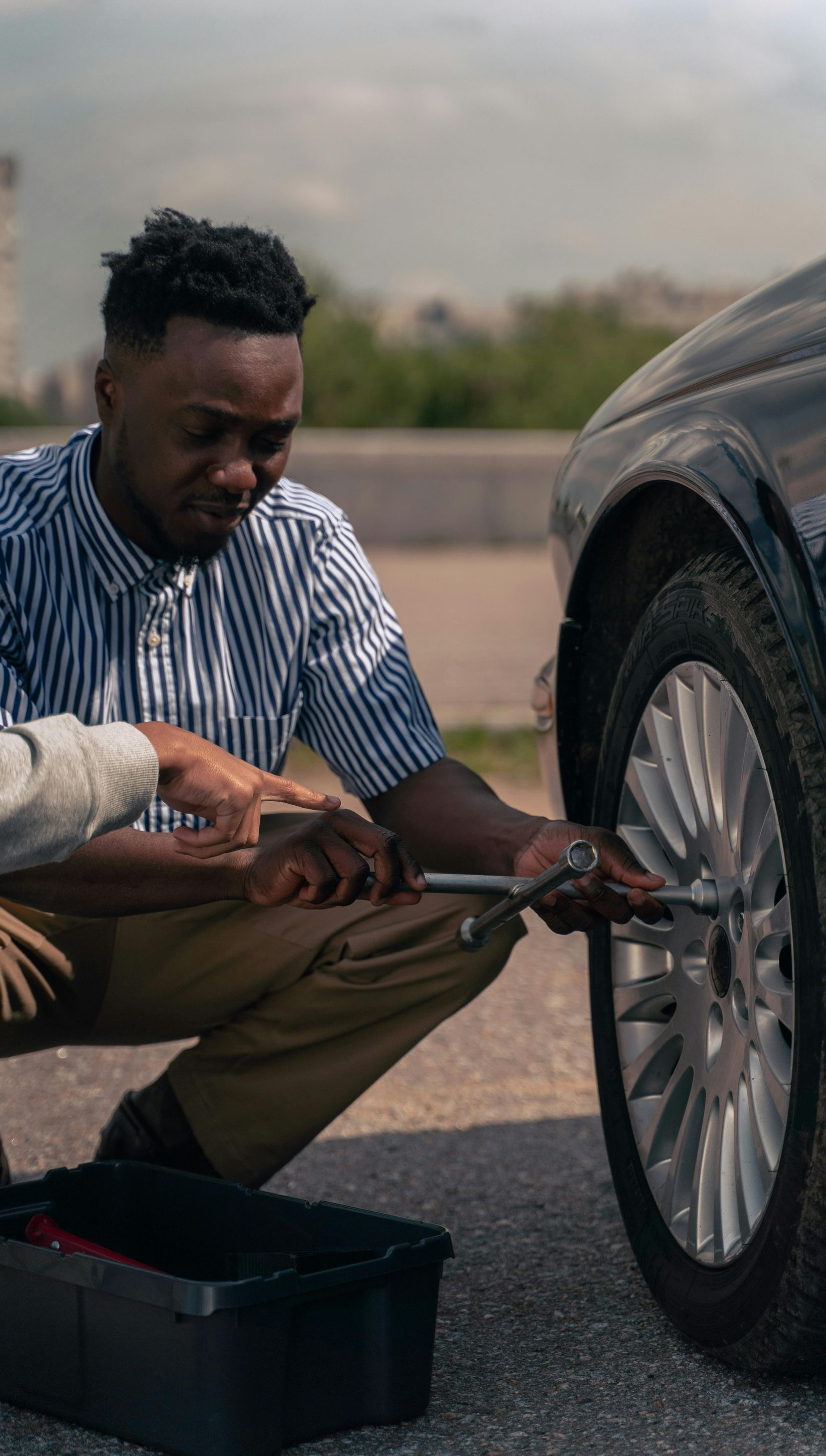 Man crouches next to a car, using a wrench. A toolbox is on the ground.