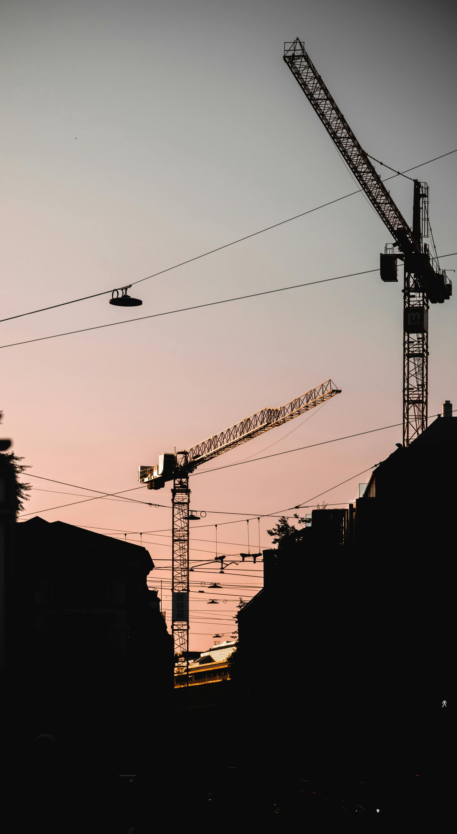 Silhouette of city skyline at sunset with three construction cranes.