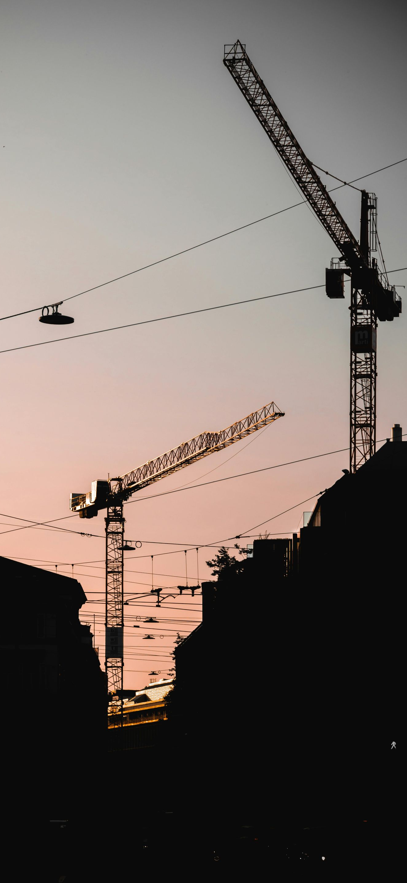 Silhouette of city skyline at sunset with three construction cranes.