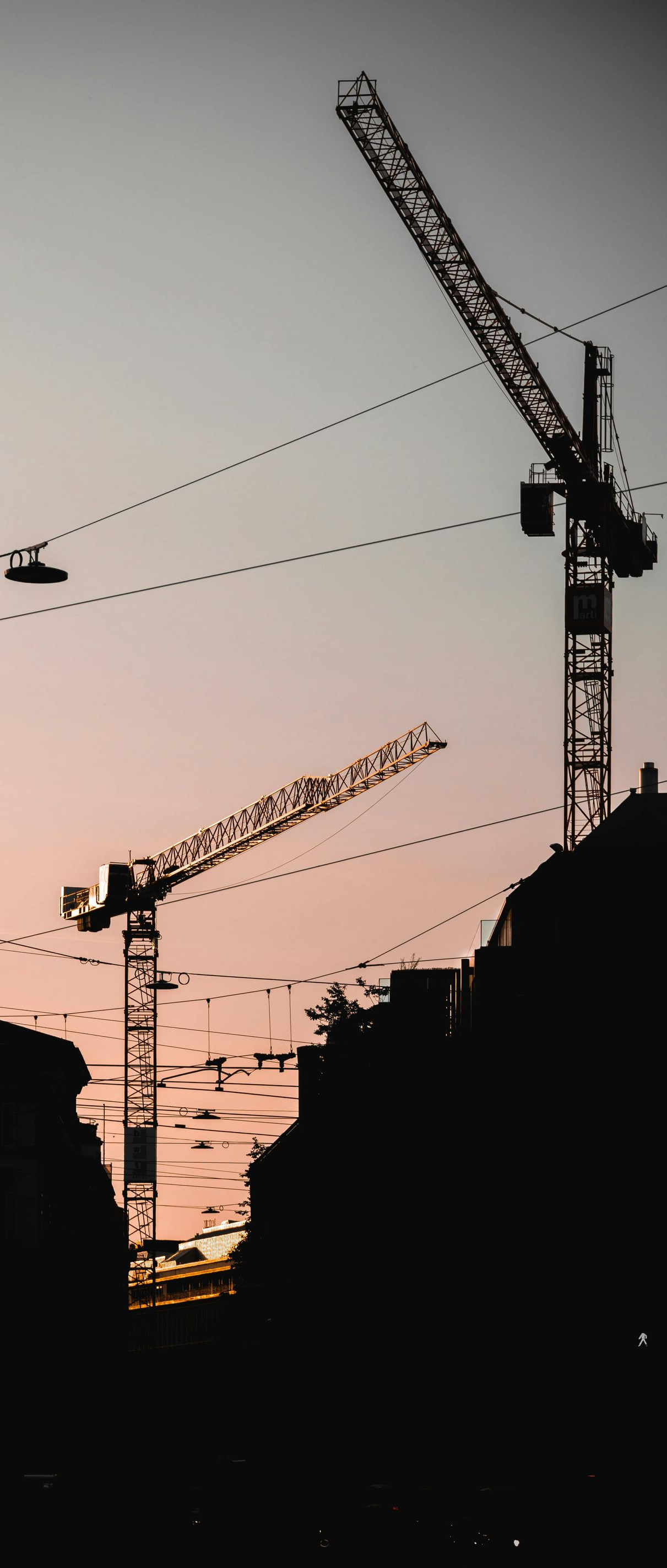 Silhouette of city skyline at sunset with three construction cranes.