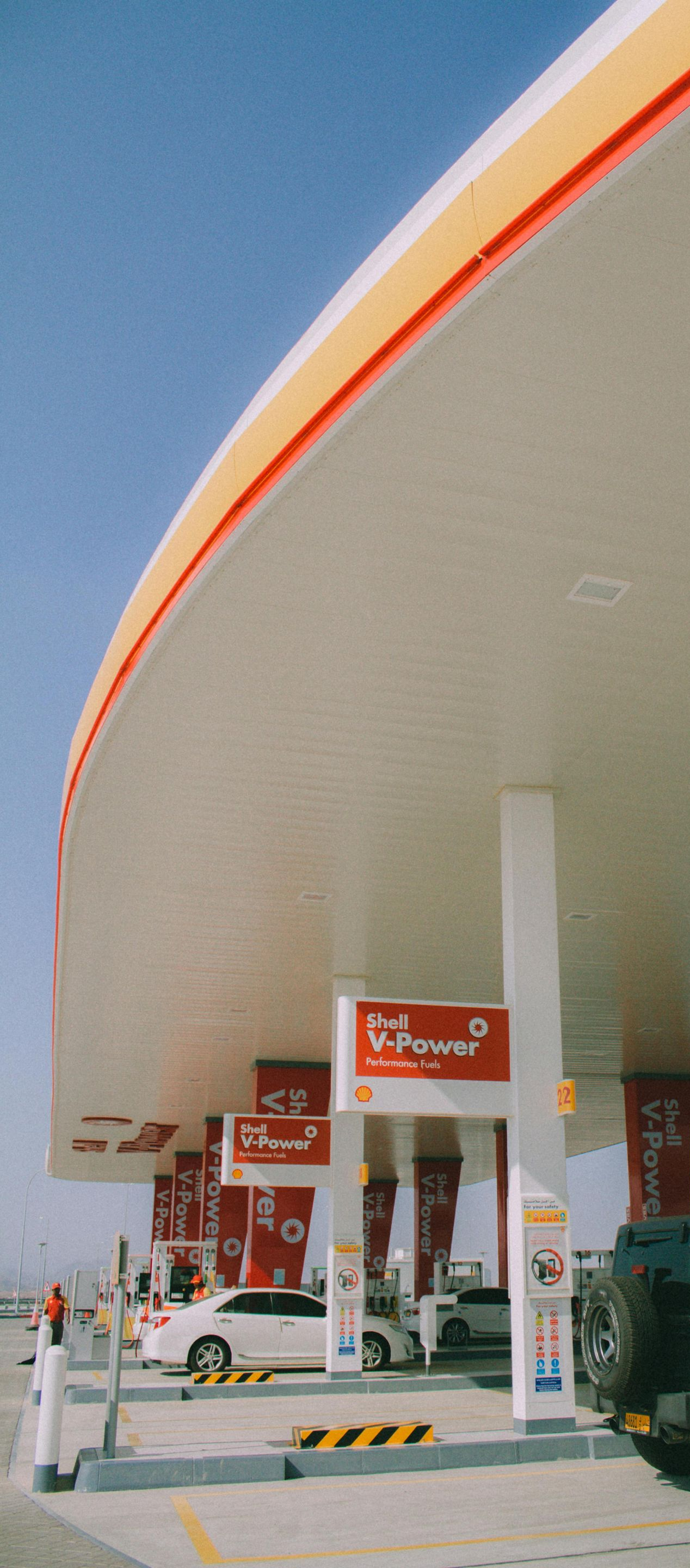 A Shell gas station canopy with cars filling up on a sunny day.