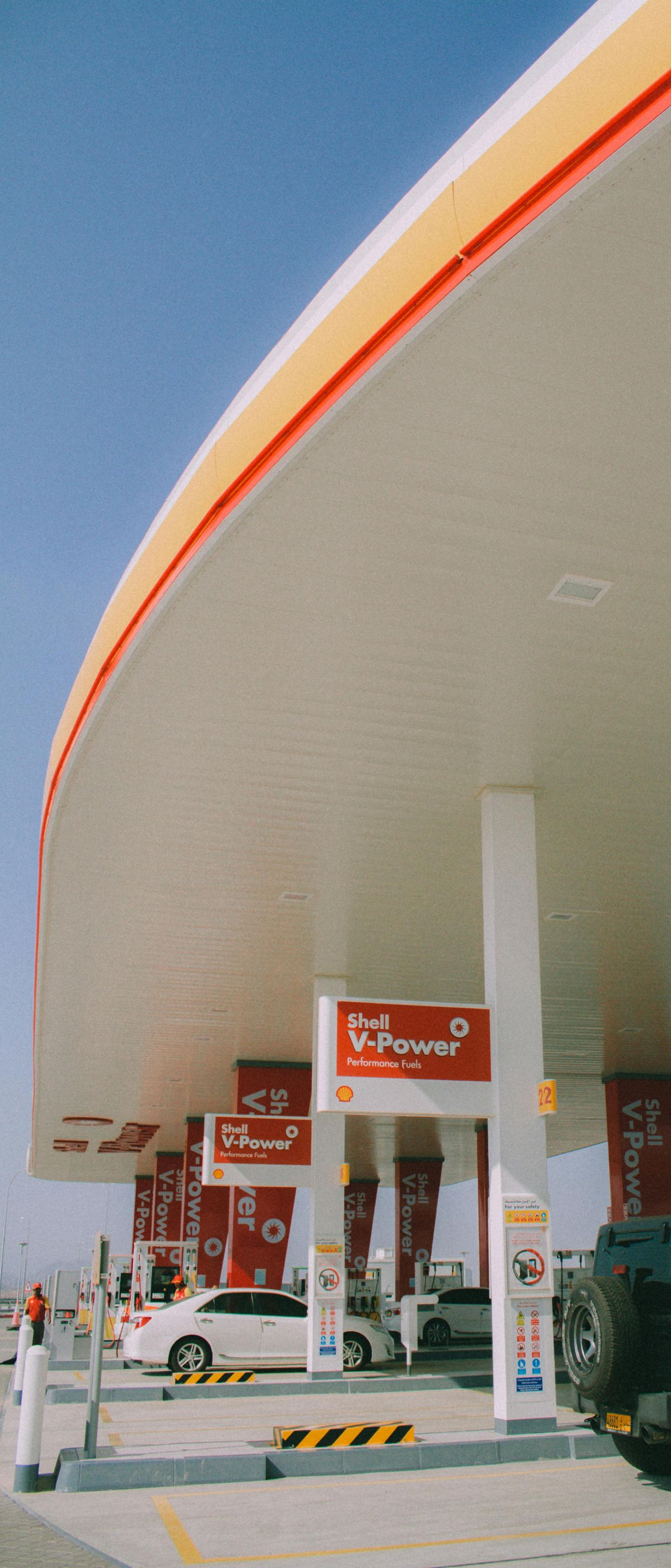 A Shell gas station canopy with cars filling up on a sunny day.