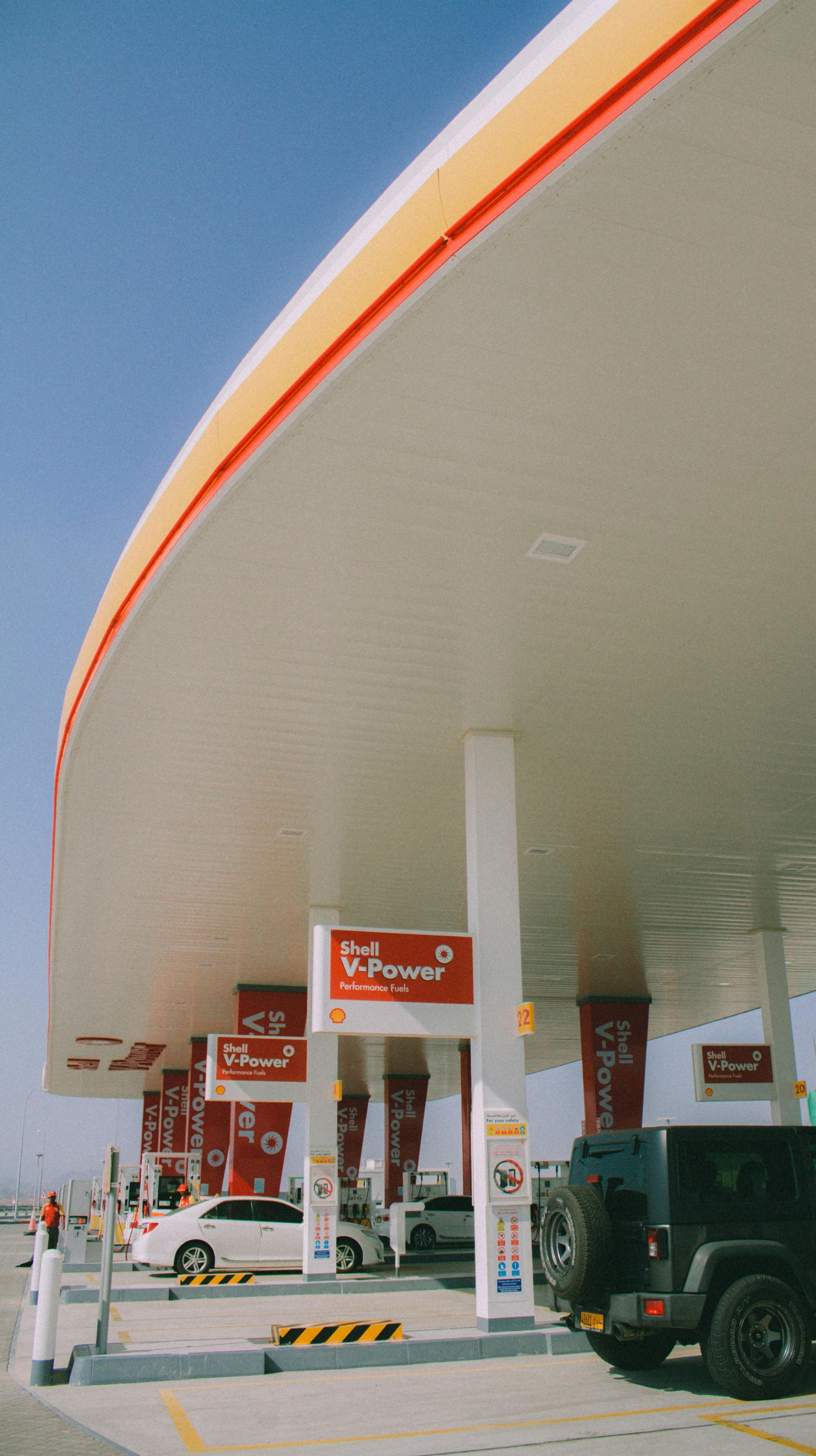 A Shell gas station canopy with cars filling up on a sunny day.