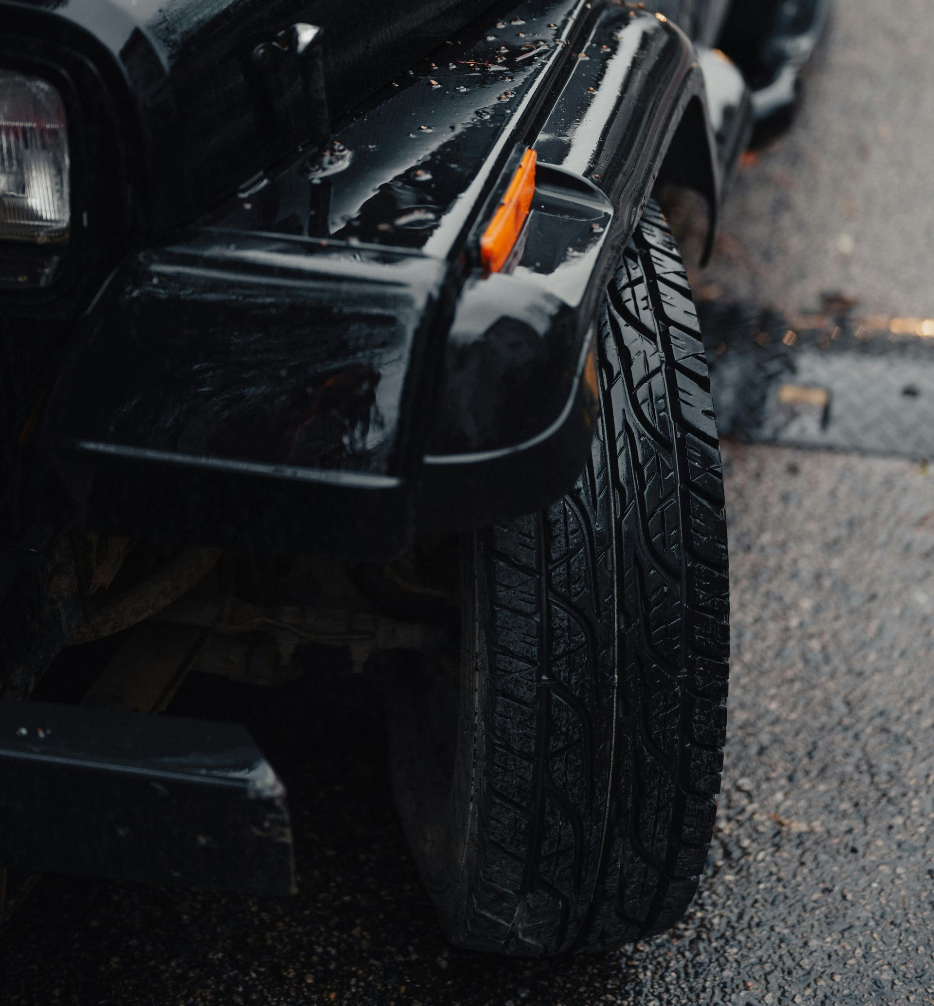 Black Jeep Wrangler, wet from rain, parked on asphalt.
