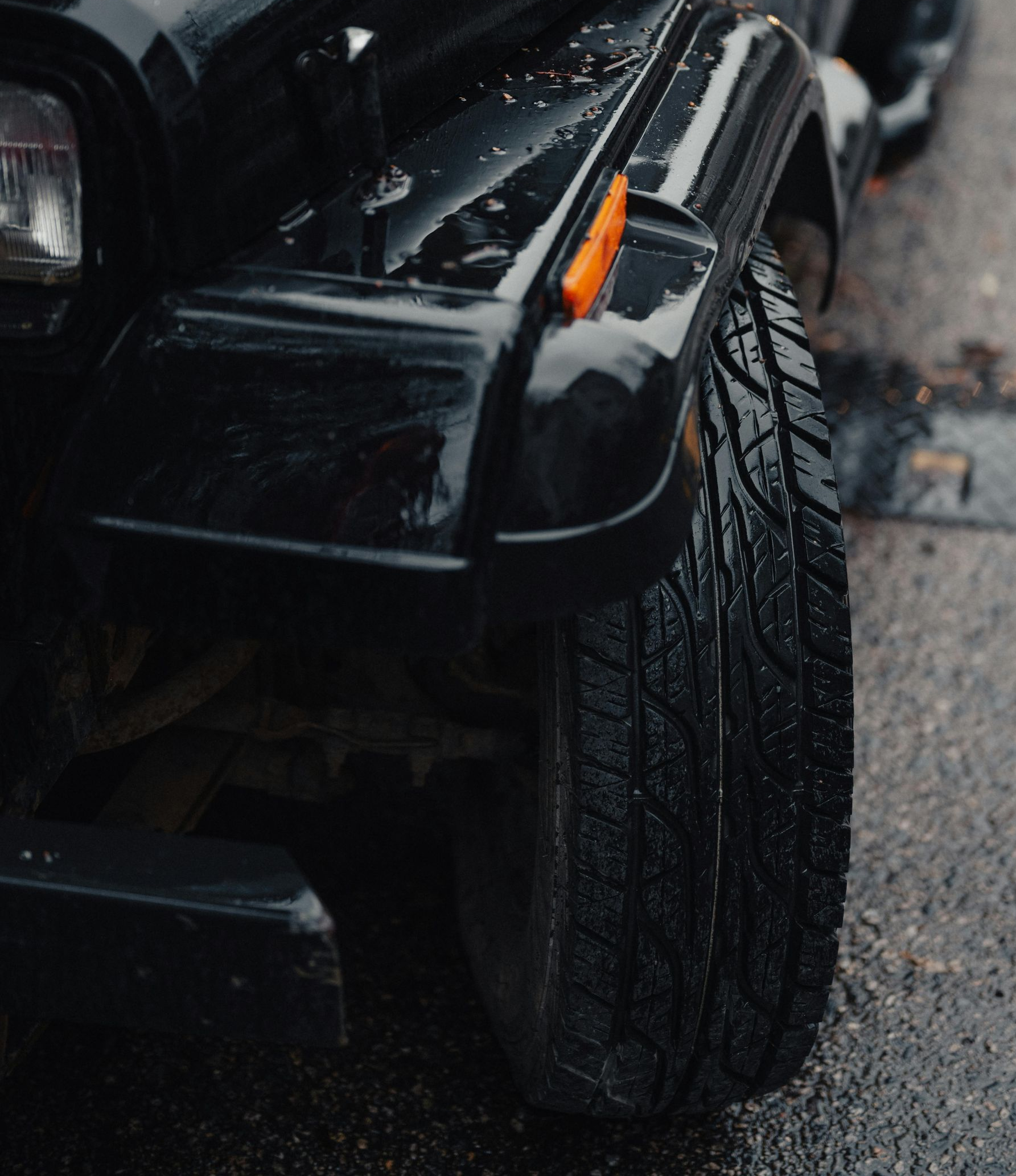 Black Jeep Wrangler, wet from rain, parked on asphalt.