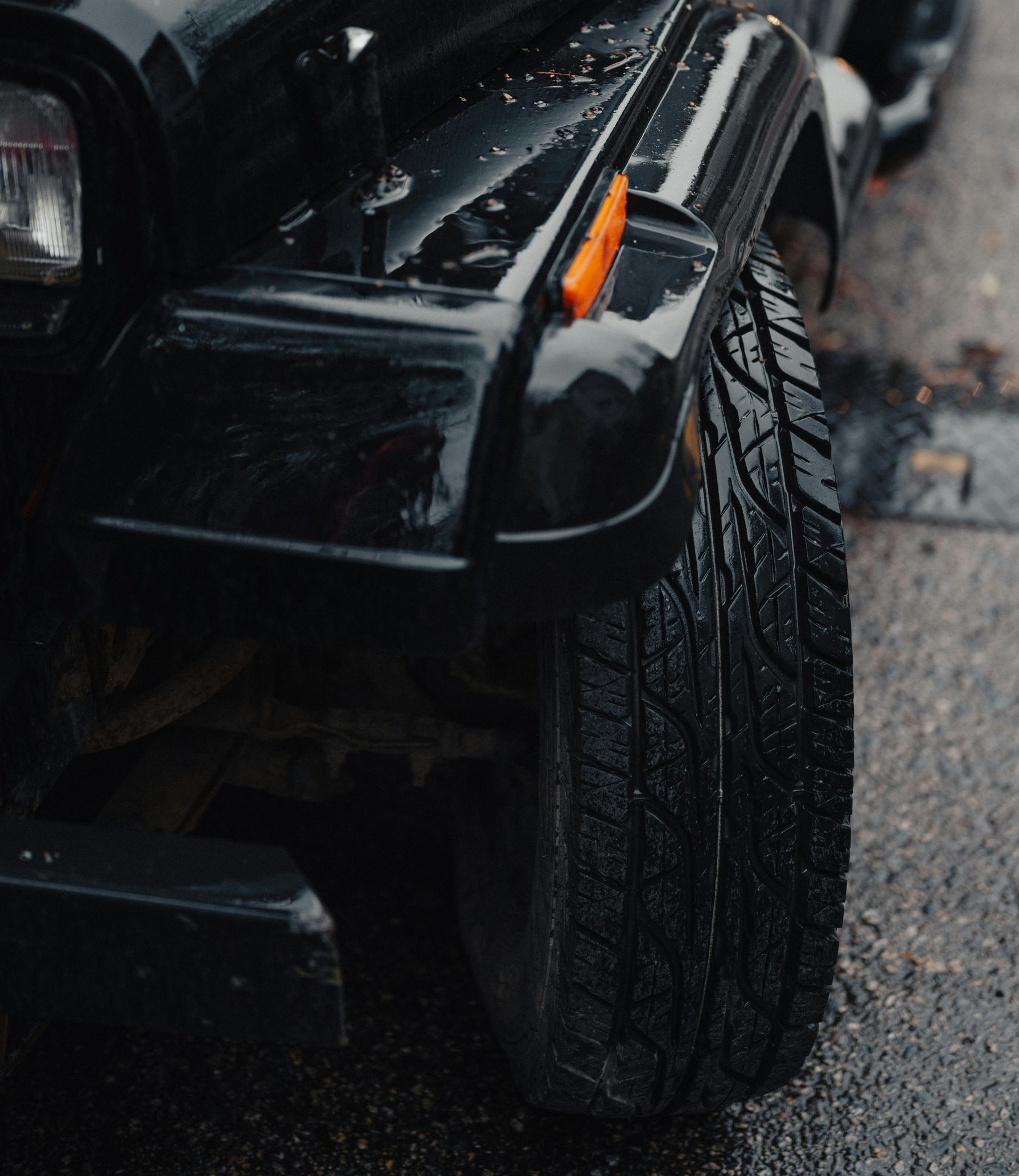 Black Jeep Wrangler, wet from rain, parked on asphalt.