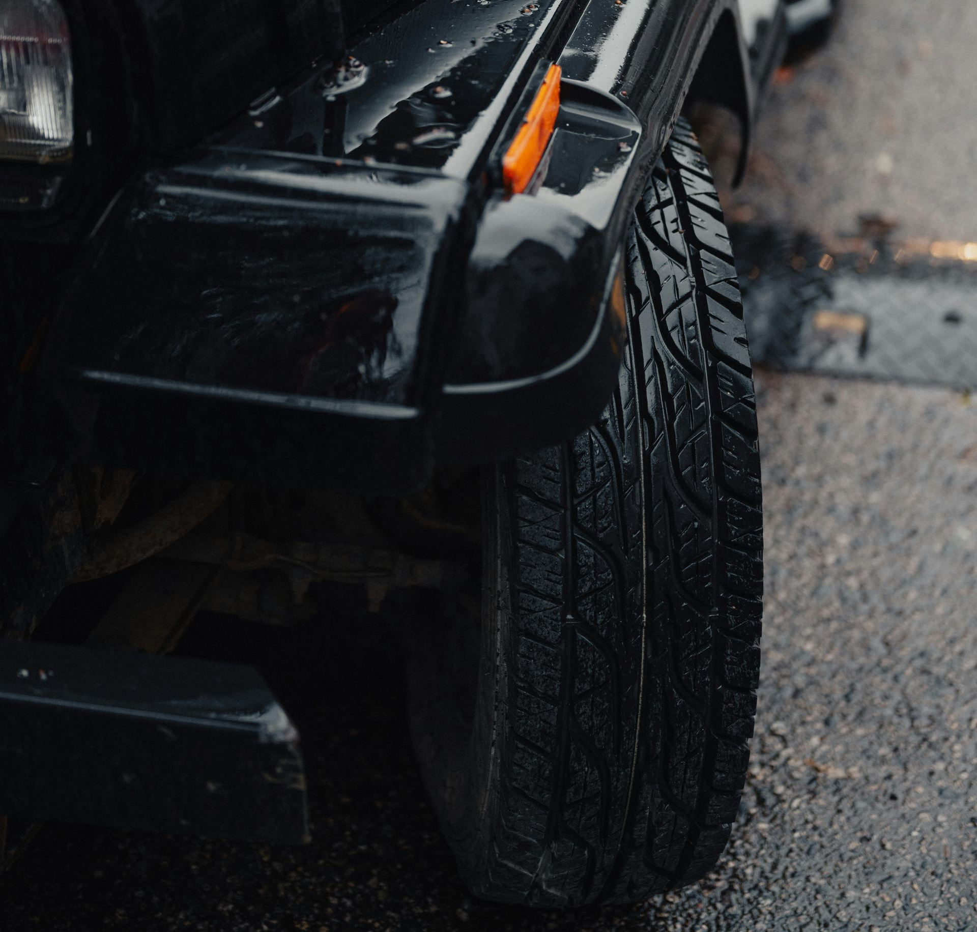 Black Jeep Wrangler, wet from rain, parked on asphalt.