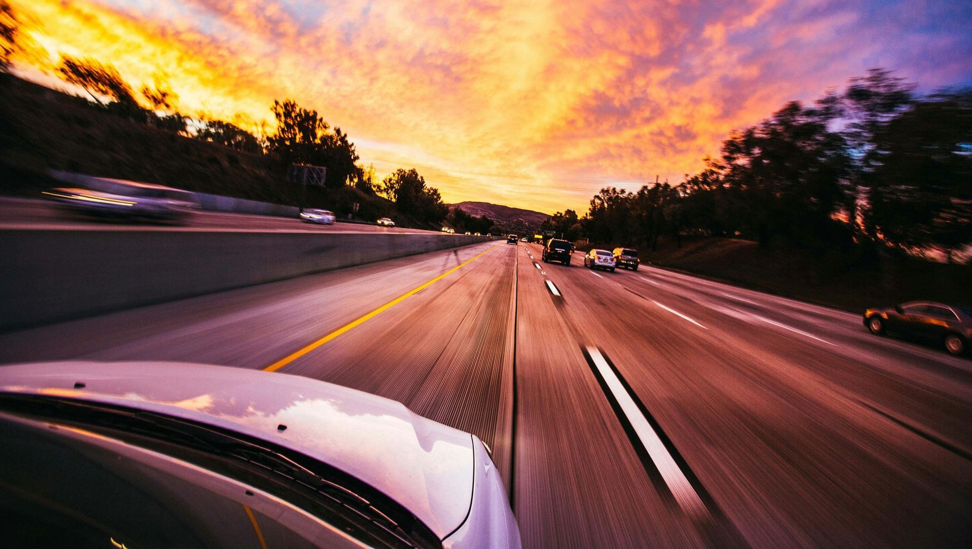 A car is driving down a highway at sunset.