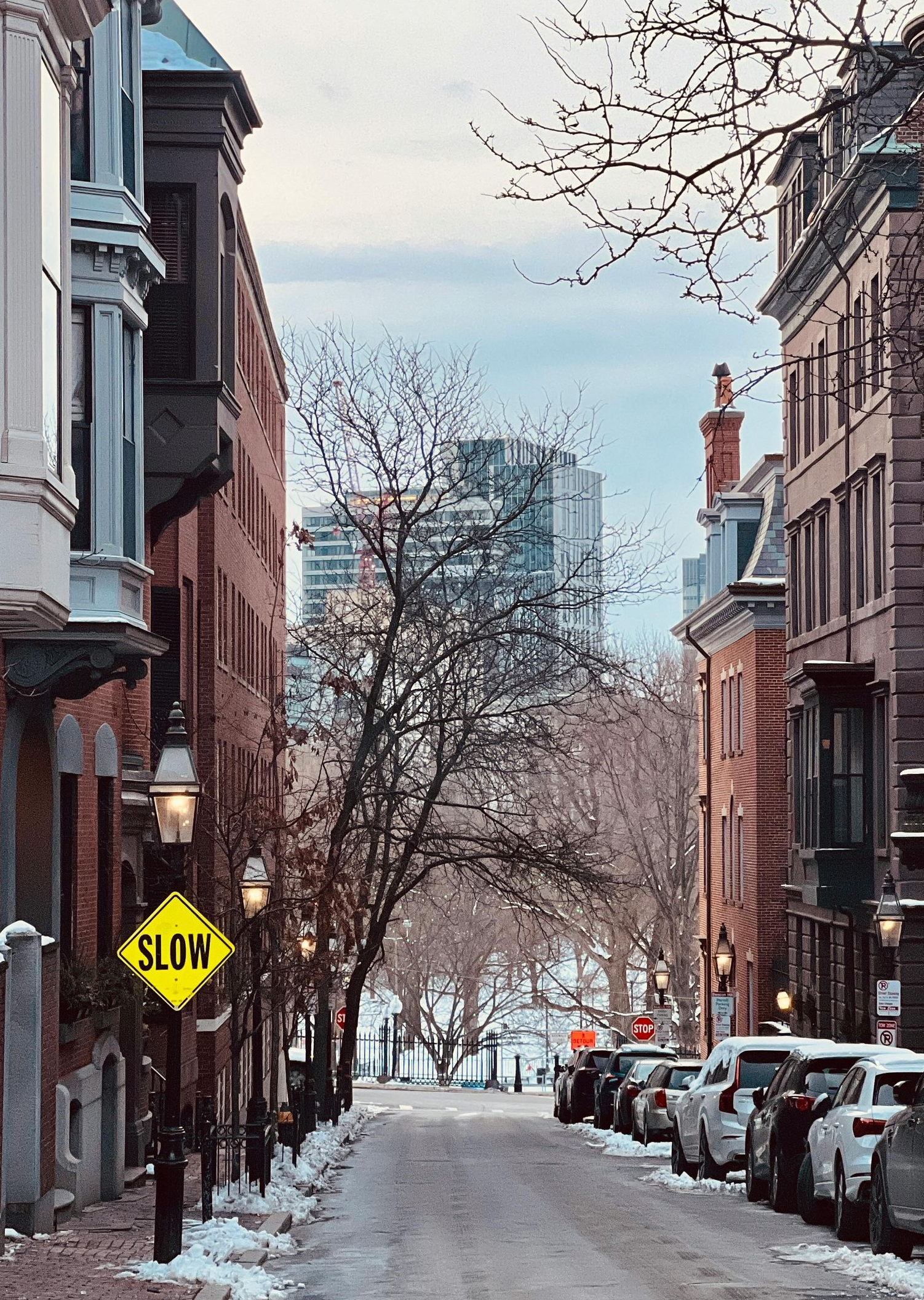 Snowy city street lined with brick buildings, parked cars, and a