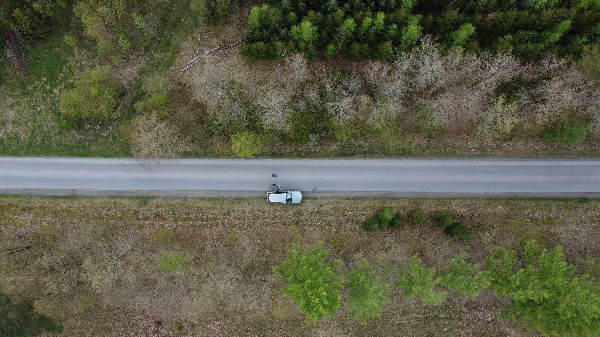 Aerial view of a road with a white van parked on it, surrounded by trees and fields.