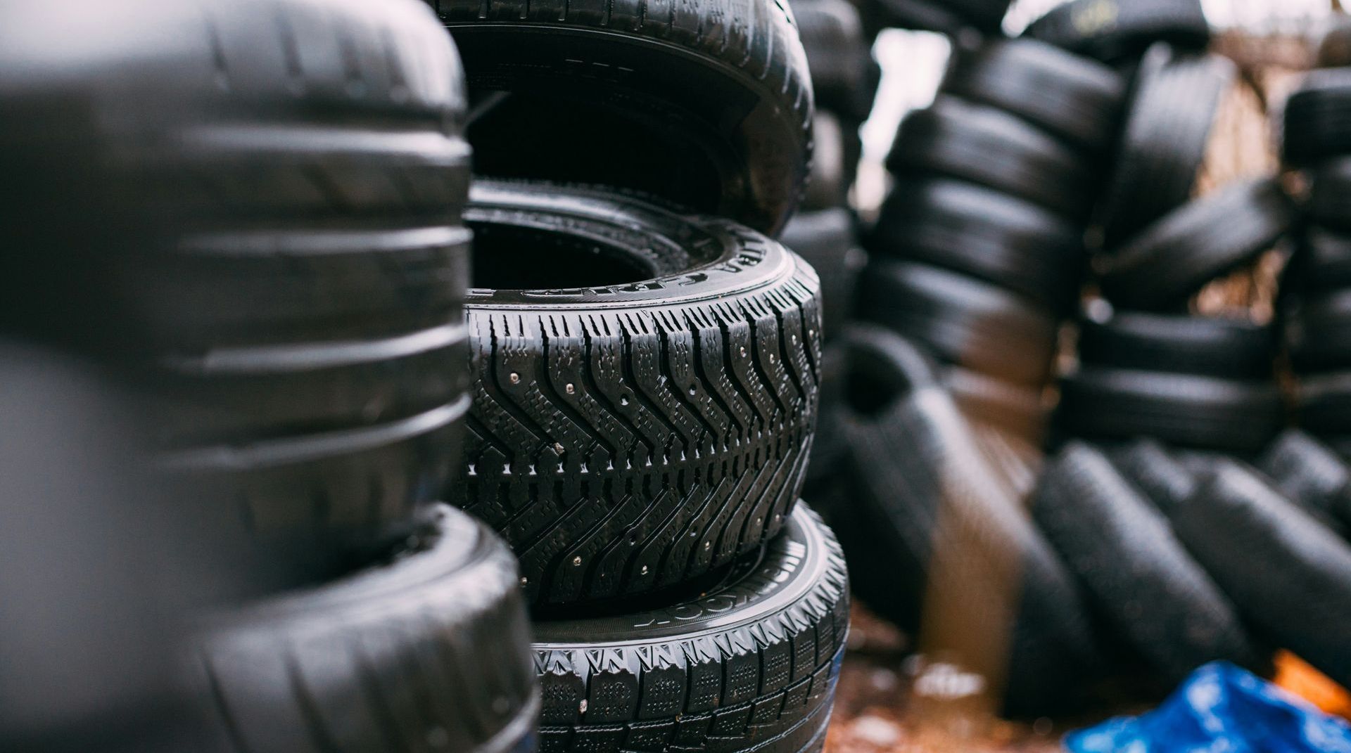 Stacks of black tires, wet with water droplets, likely outdoors. Some tires have visible tread patterns.