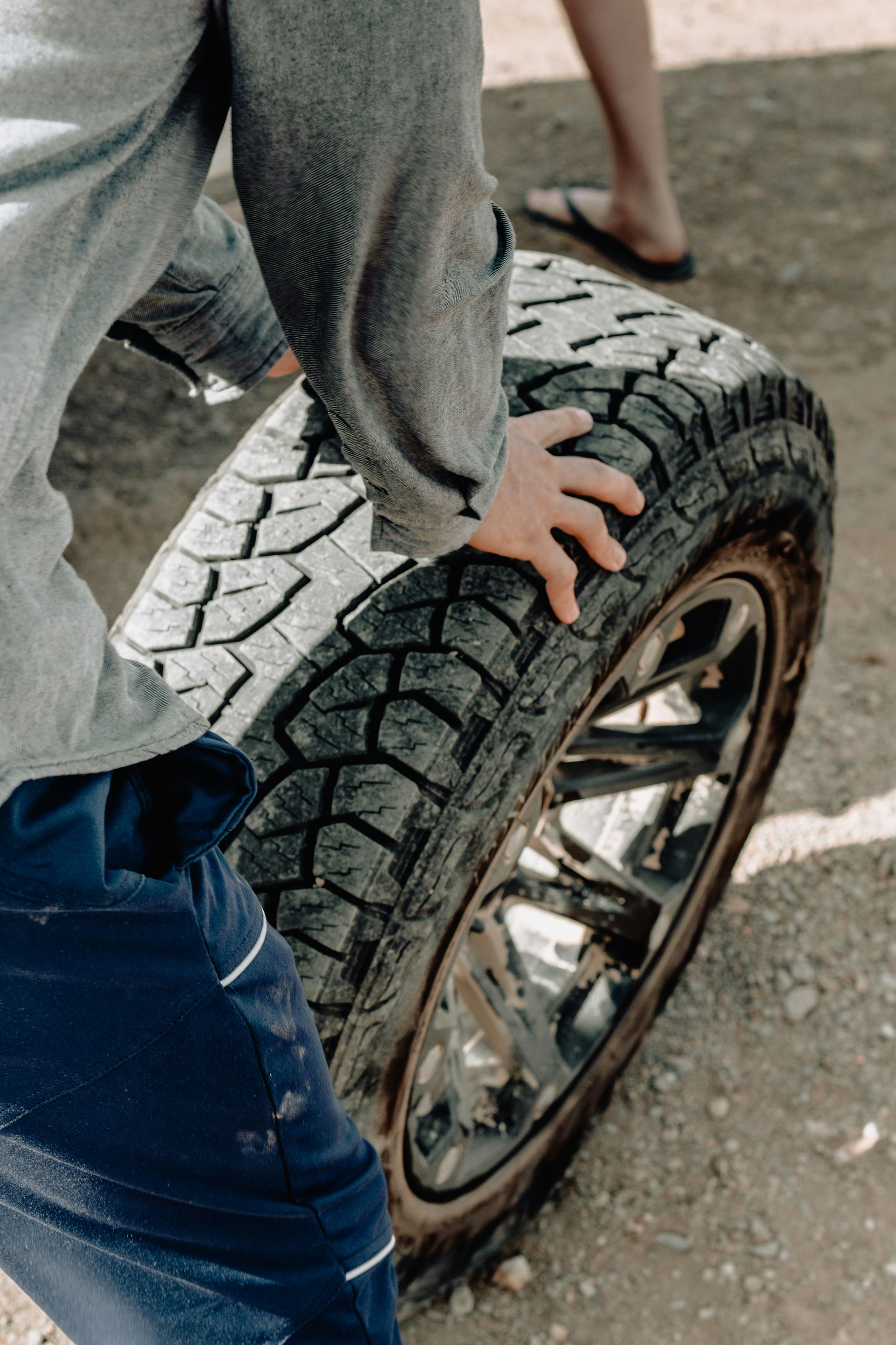 Person gripping a large tire with a shiny chrome rim outdoors.