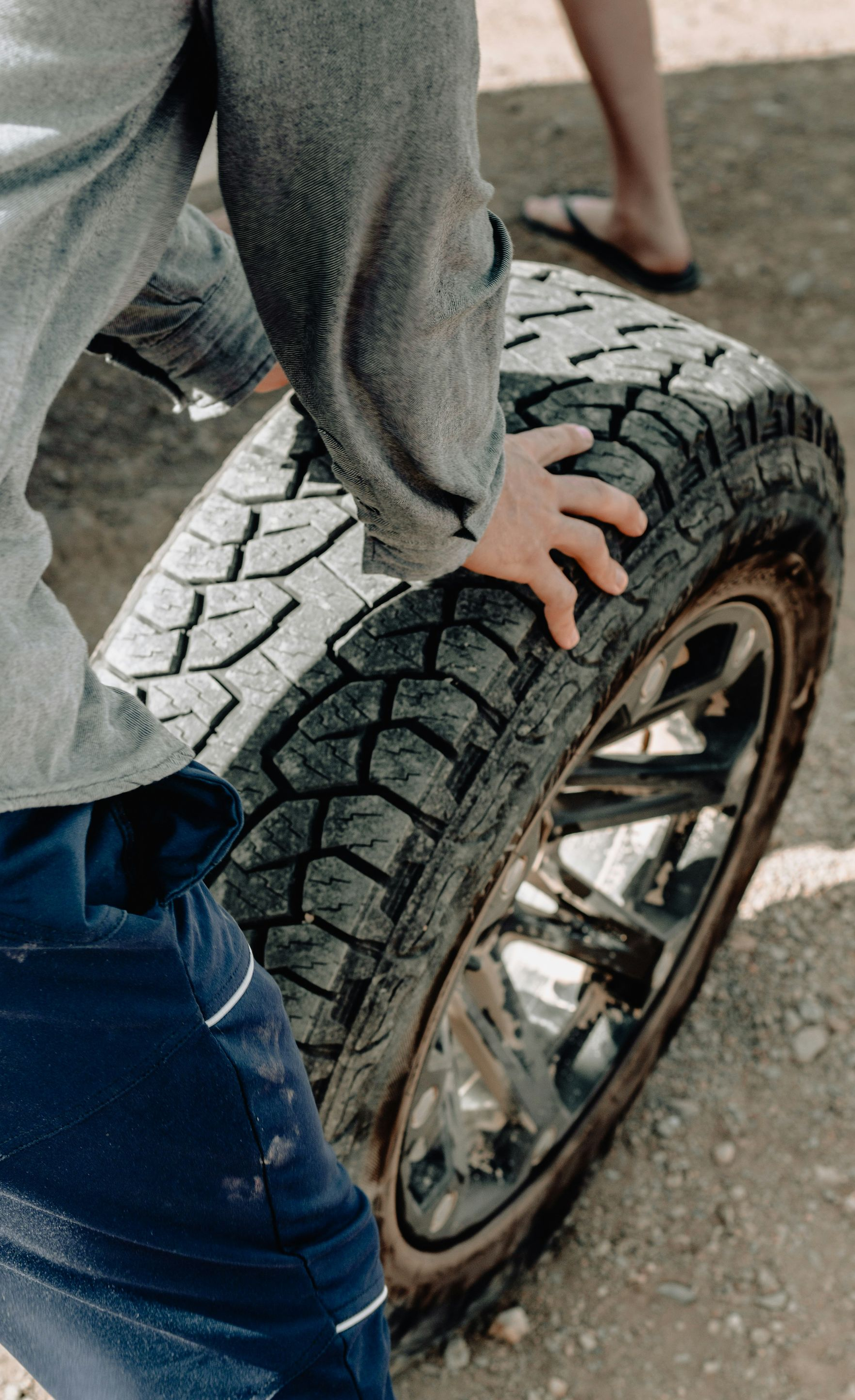 Person gripping a large tire with a shiny chrome rim outdoors.