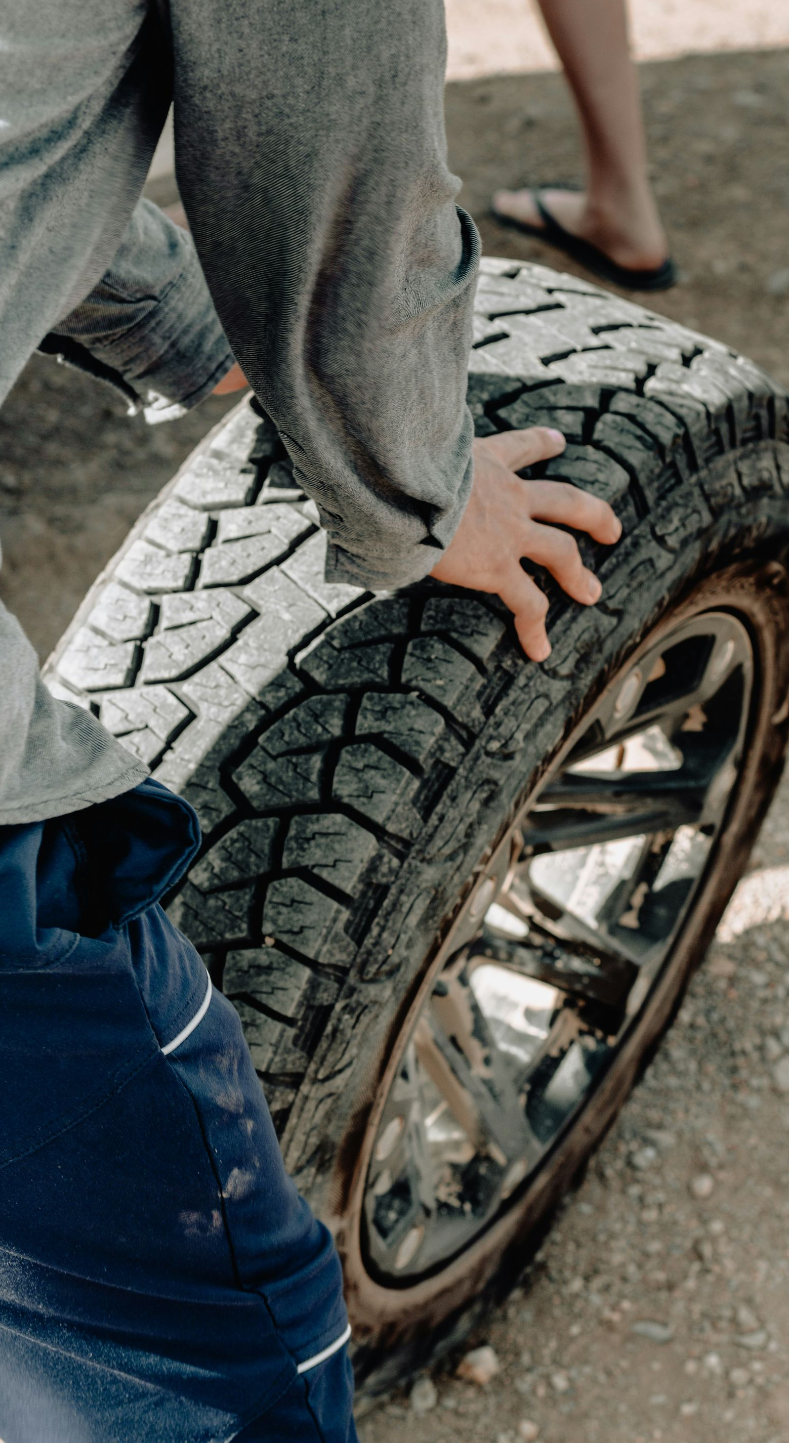 Person gripping a large tire with a shiny chrome rim outdoors.
