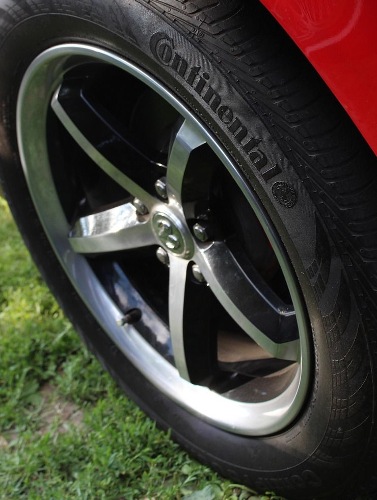 Black and silver car wheel with Continental tire, set on green grass.