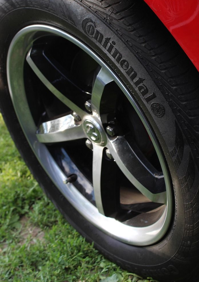 Black and silver car wheel with Continental tire, set on green grass.