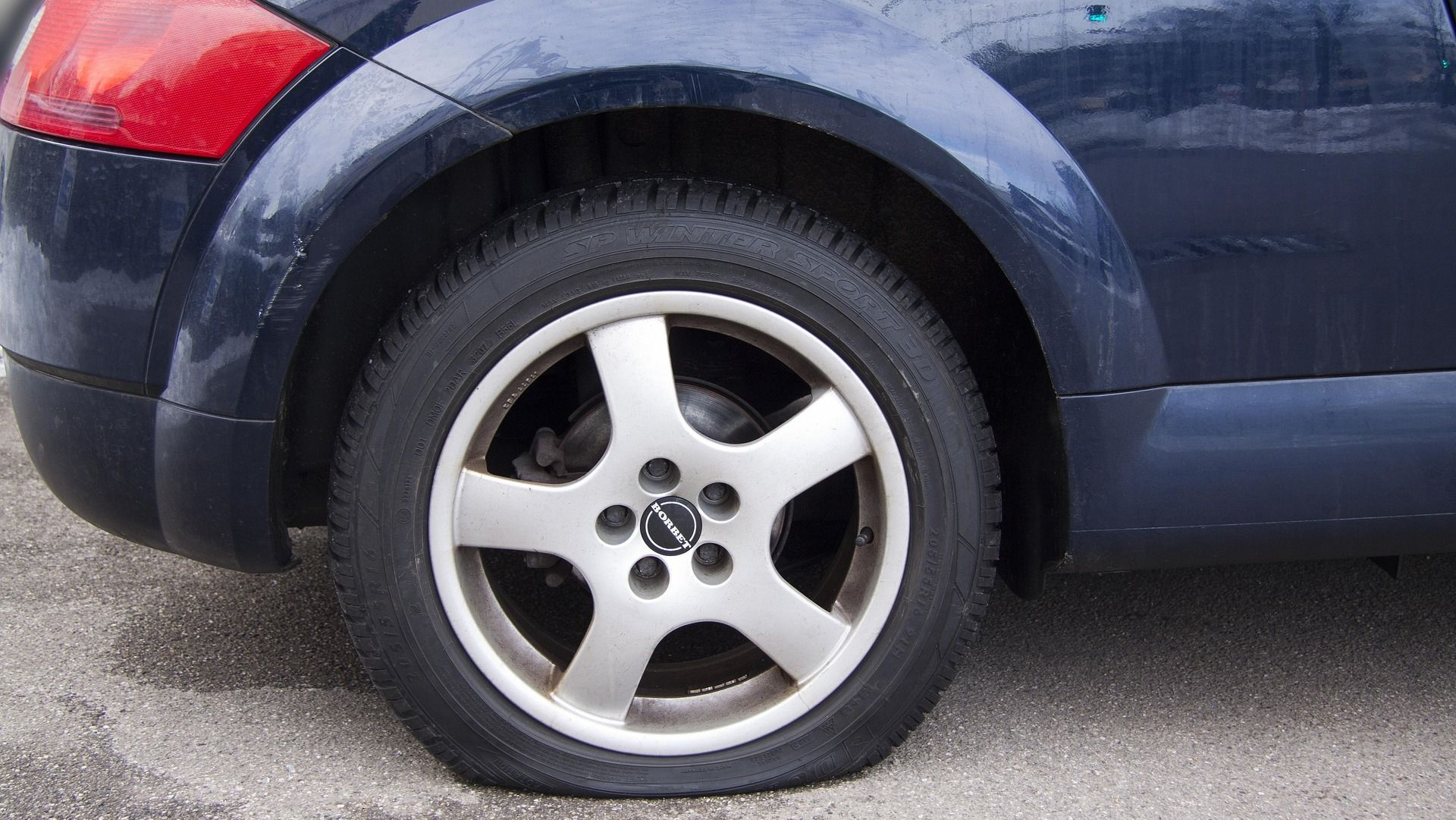 Flat tire on a dark blue car, showing the wheel and part of the vehicle's body.