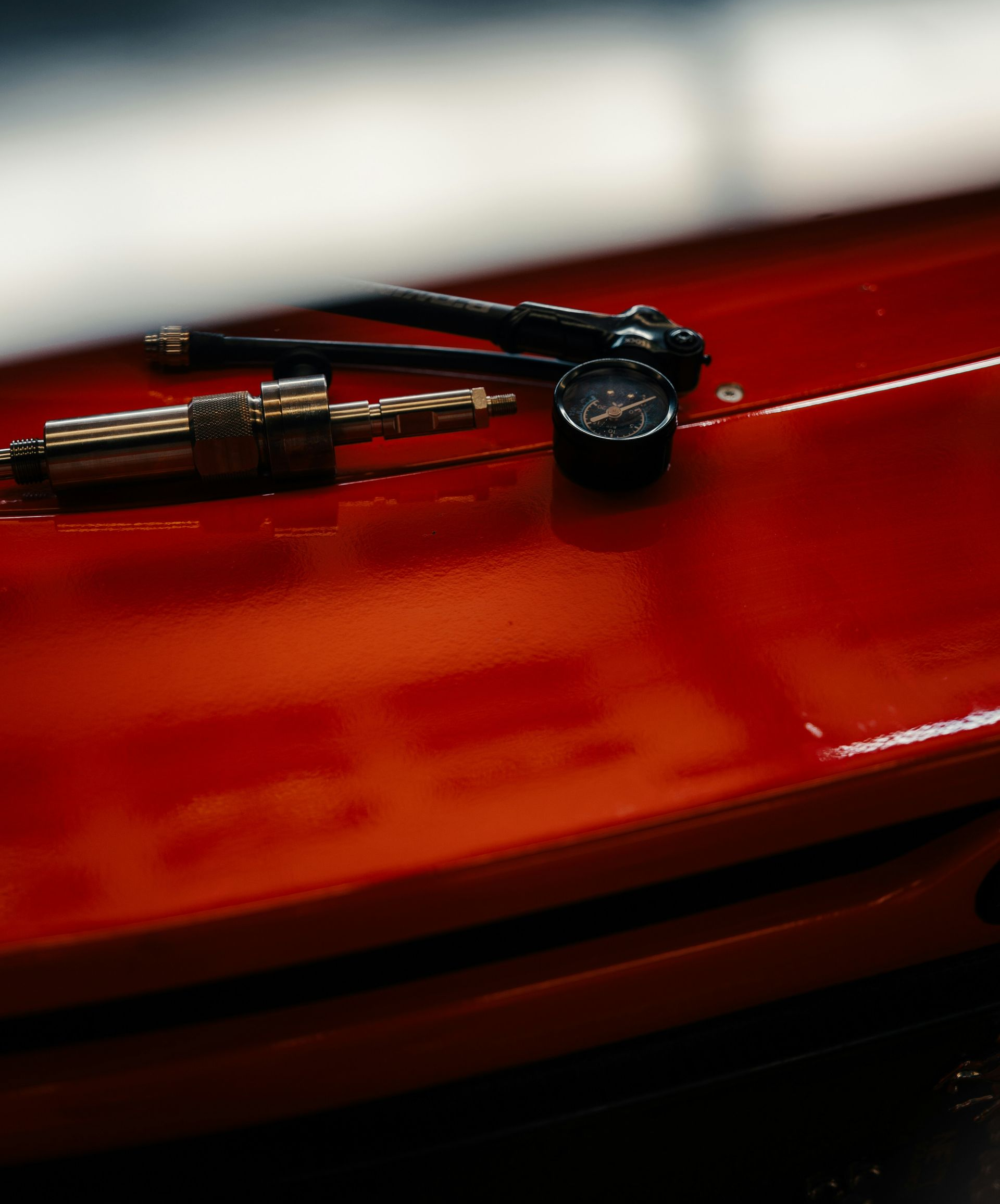 A tire pressure gauge and a valve stem tool rest on the bright red, glossy surface of a car hood.