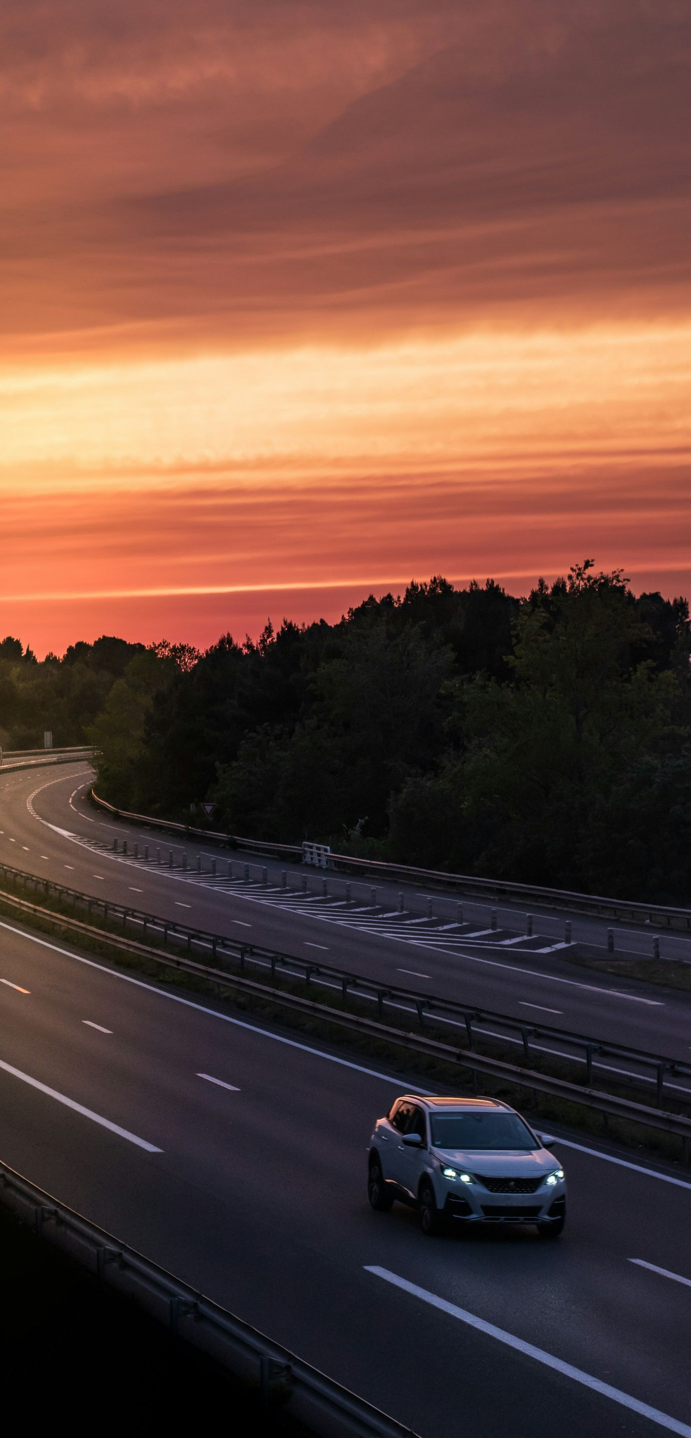 Car driving on highway at sunset. Orange and red sky above a winding road.