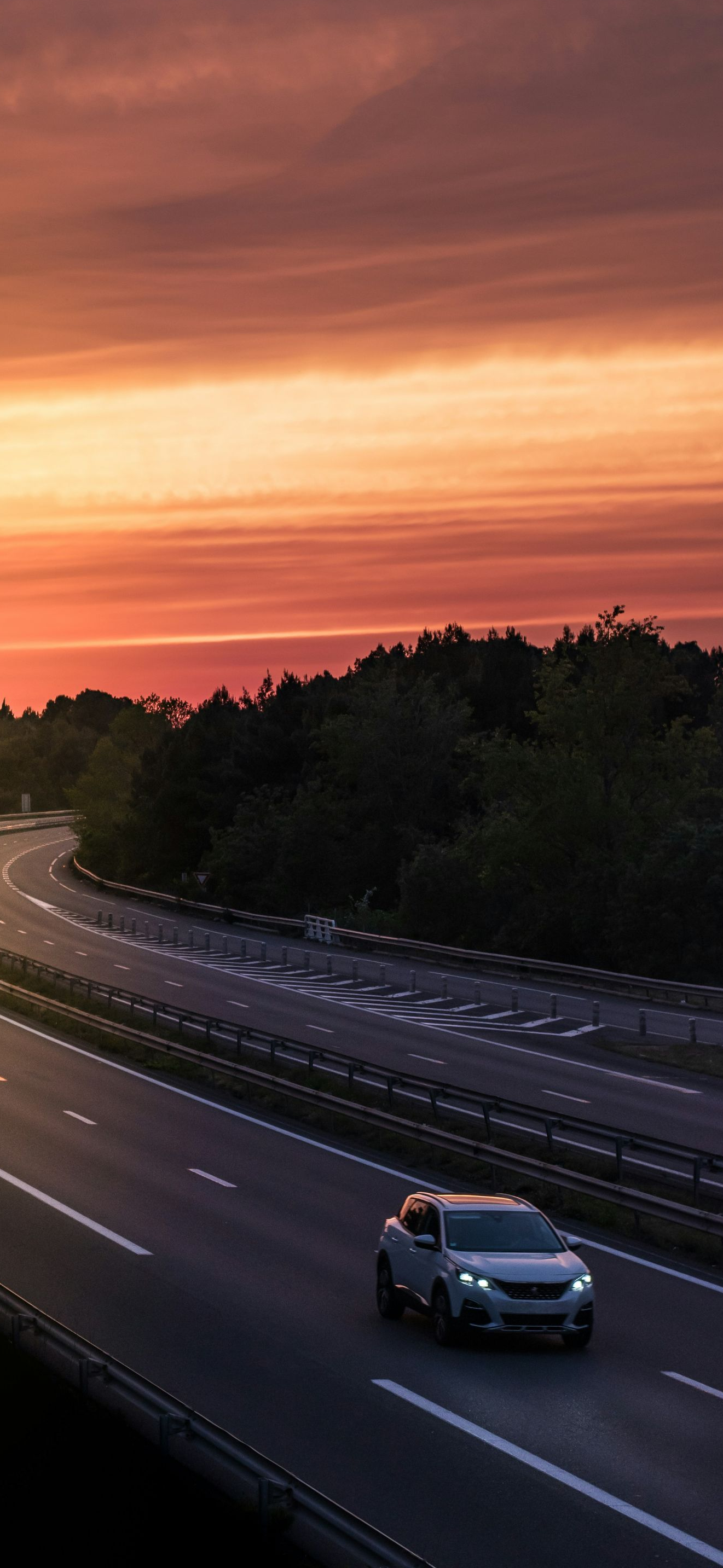 Car driving on highway at sunset. Orange and red sky above a winding road.
