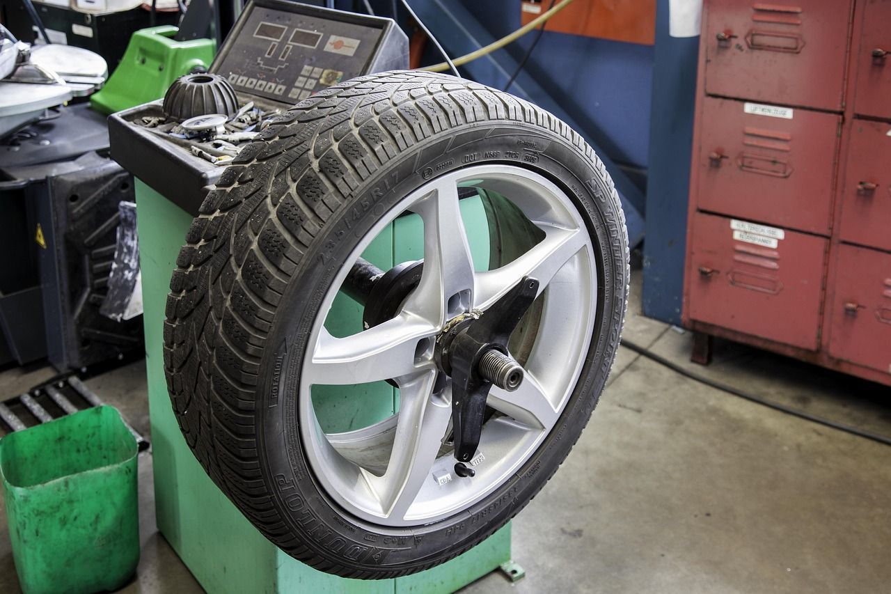 A car tire mounted on a balancing machine, indoors, a mechanic's shop setting.
