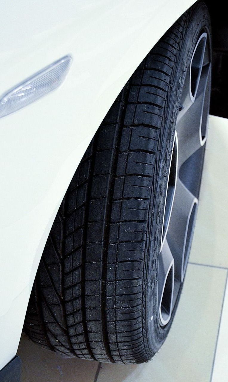 White car's front tire and alloy wheel close-up. The black tire has tread, and the wheel has a silver rim.