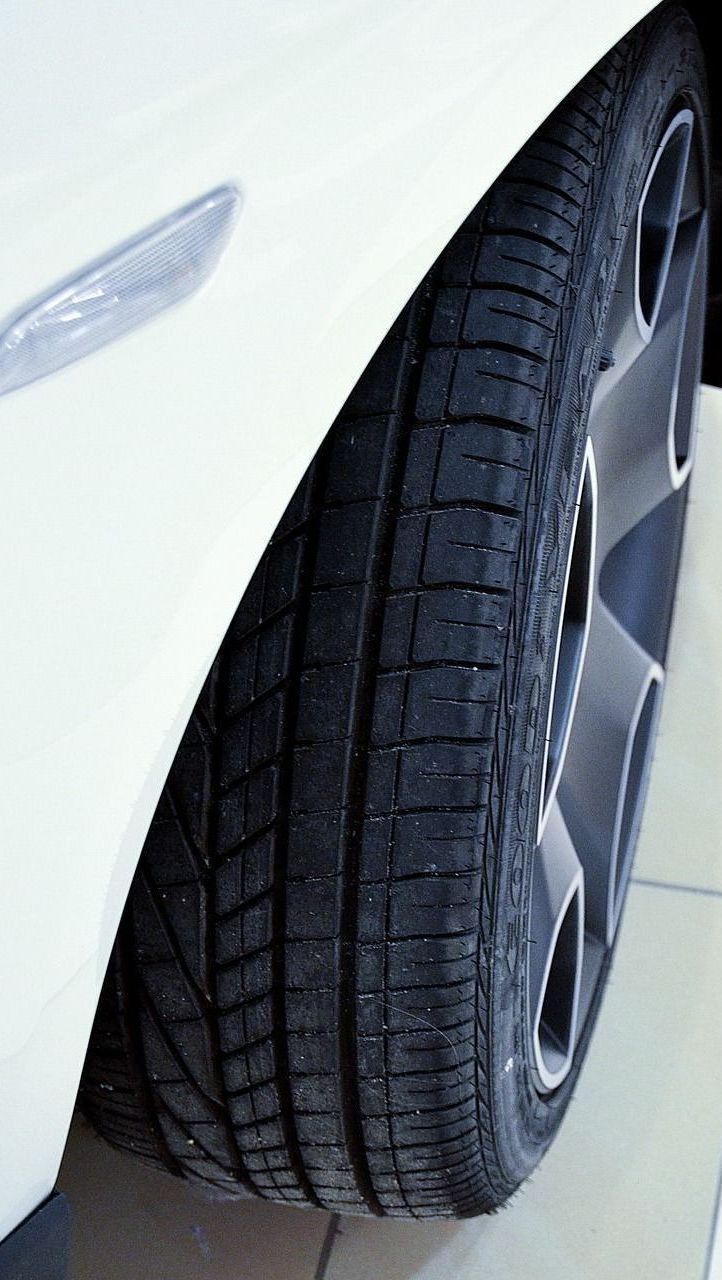 White car's front tire and alloy wheel close-up. The black tire has tread, and the wheel has a silver rim.