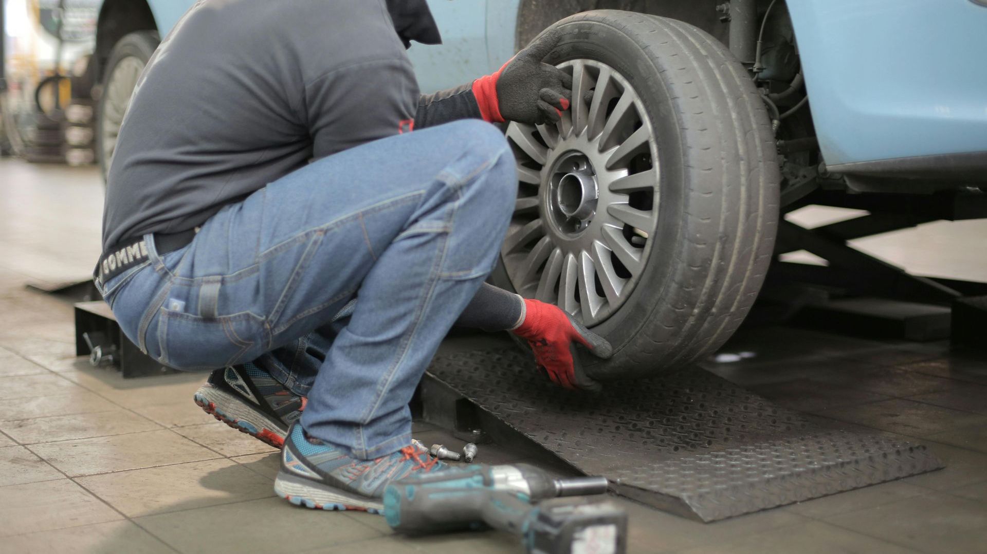 A man is kneeling down to change a tire on a car.