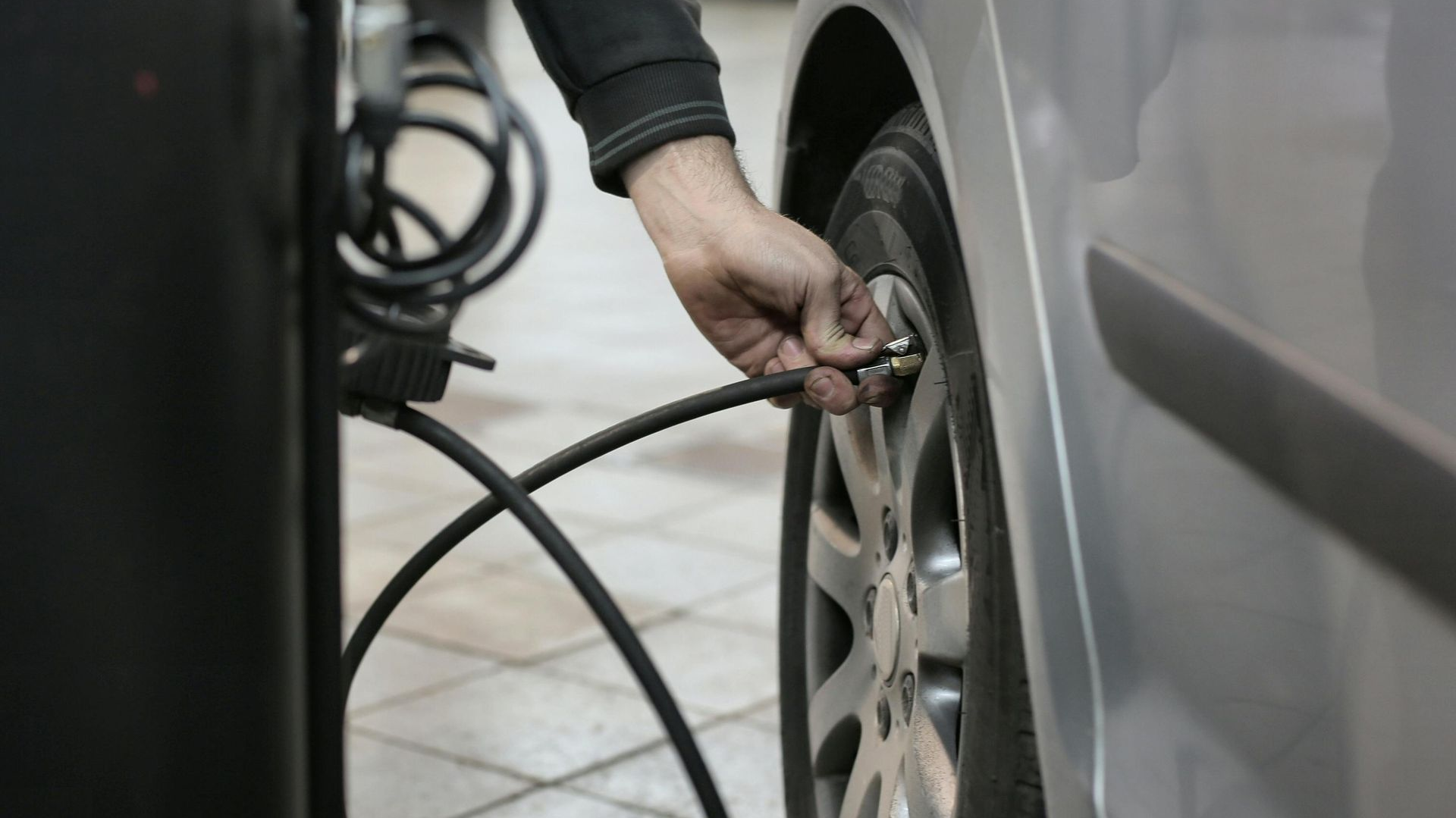 Hand inflating a car tire with an air hose at a service station.