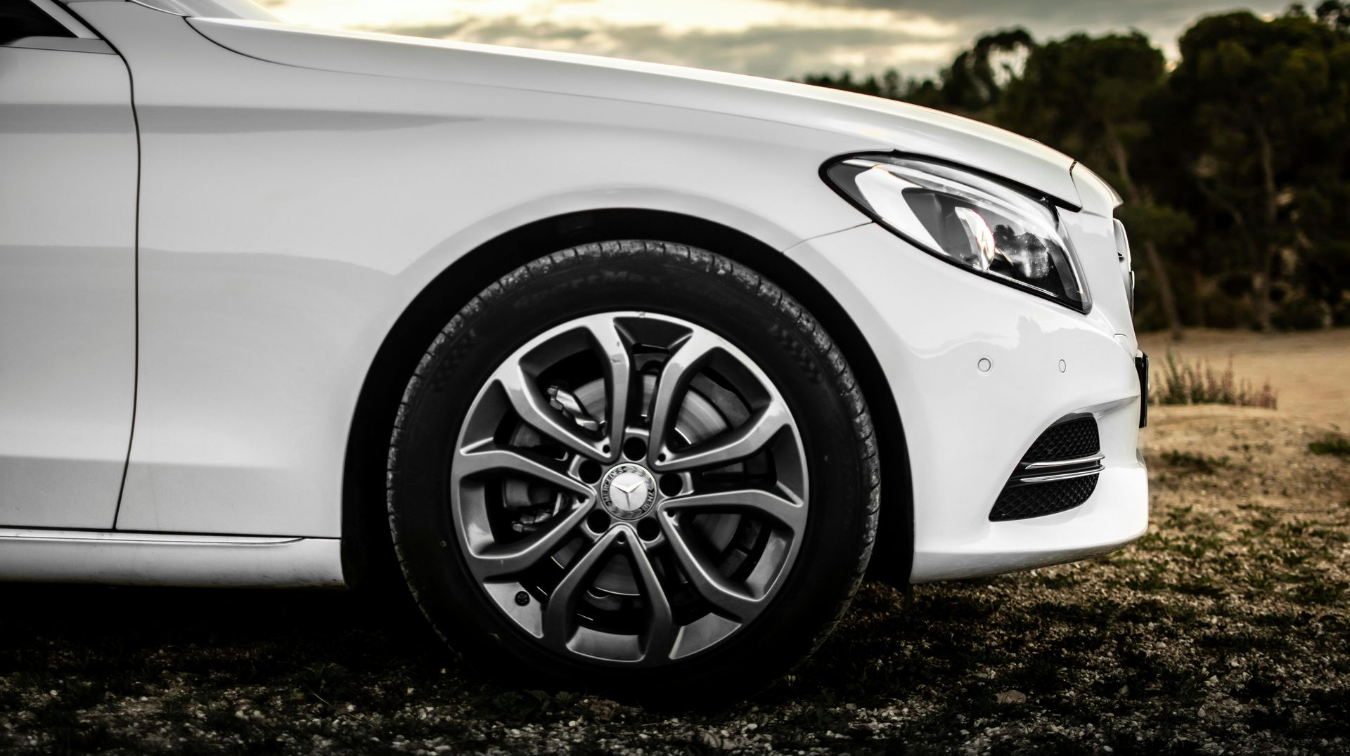 White Mercedes-Benz sedan, front view, tire and headlight visible, outdoors.