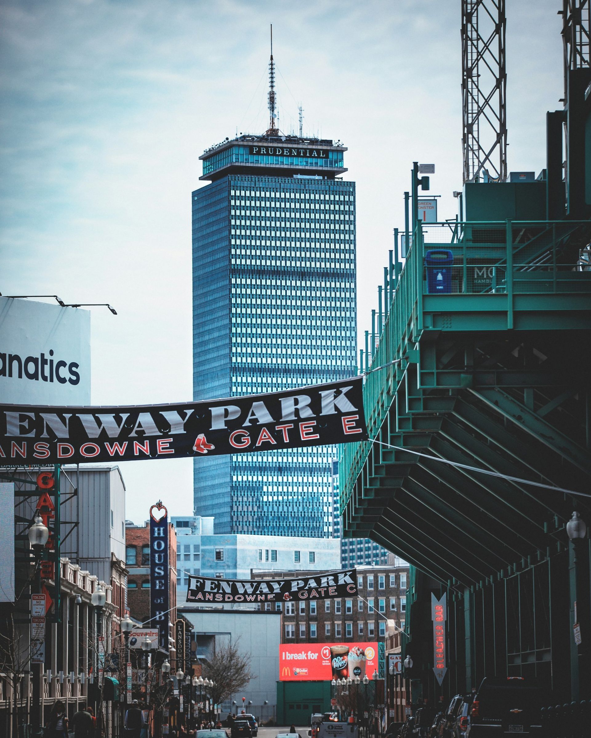 The Prudential Tower rises above Fenway Park on a street lined with banners and buildings in Boston.