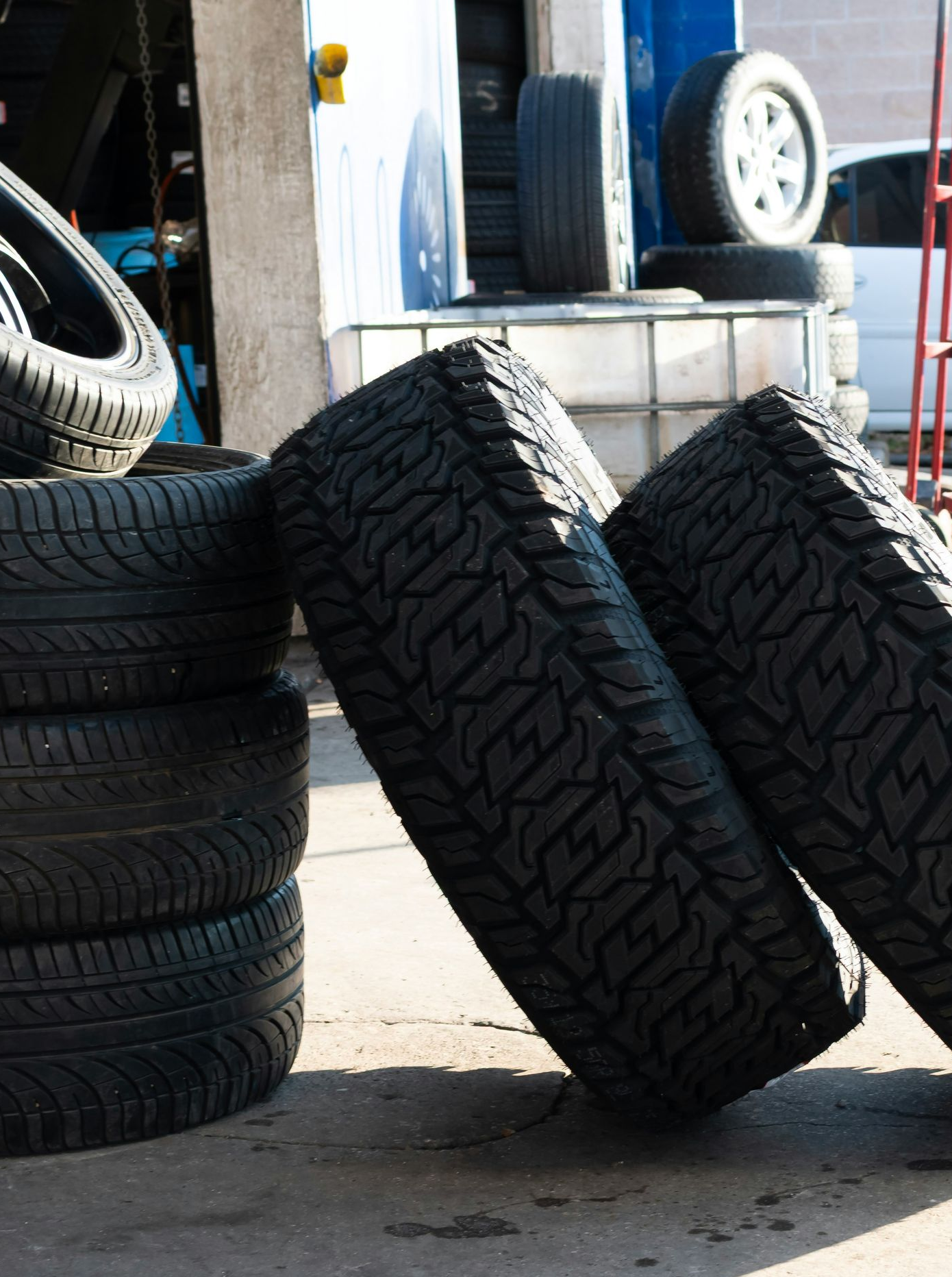 Tires stacked and leaning in a garage setting, sunlight.