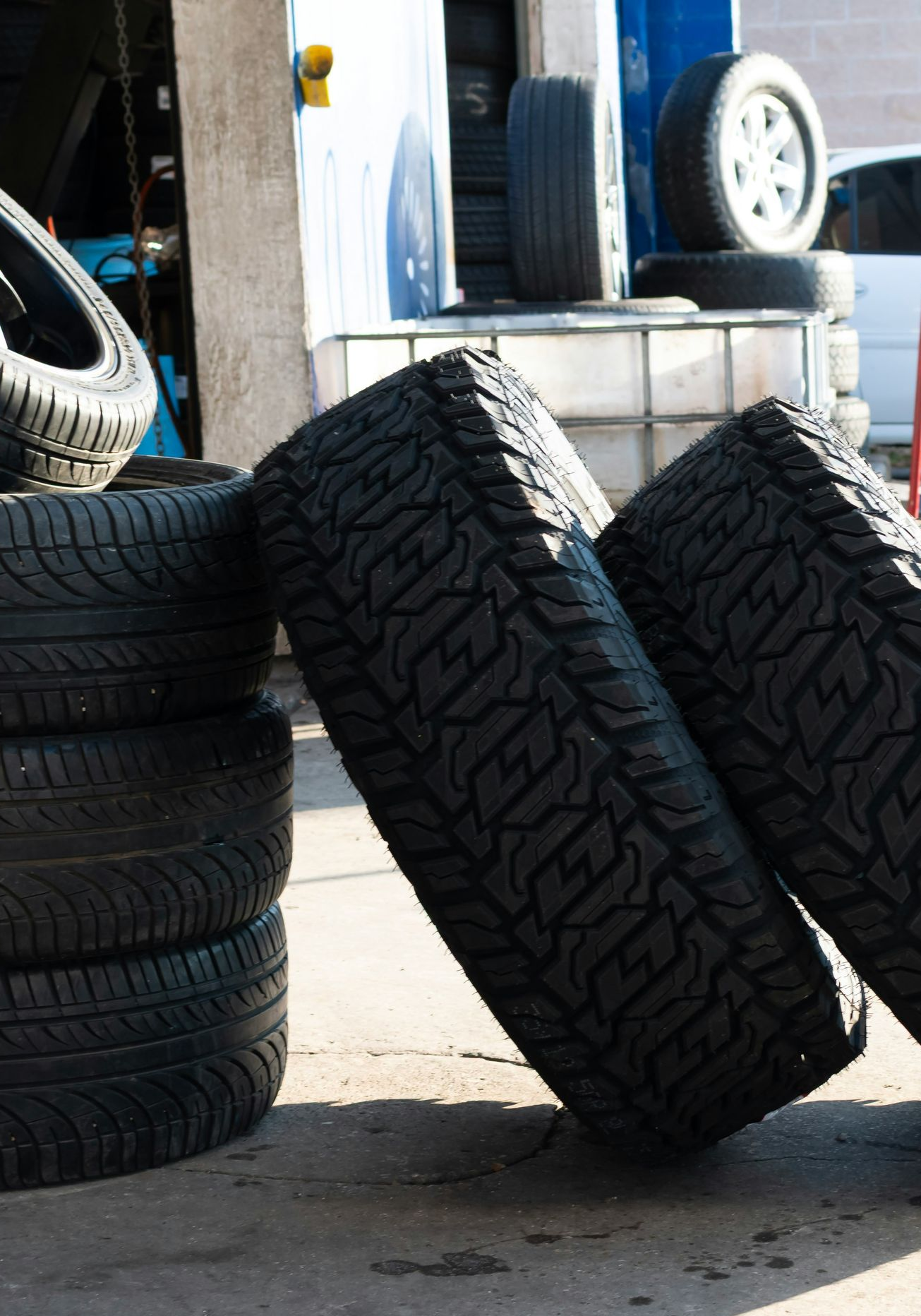 Tires stacked and leaning in a garage setting, sunlight.