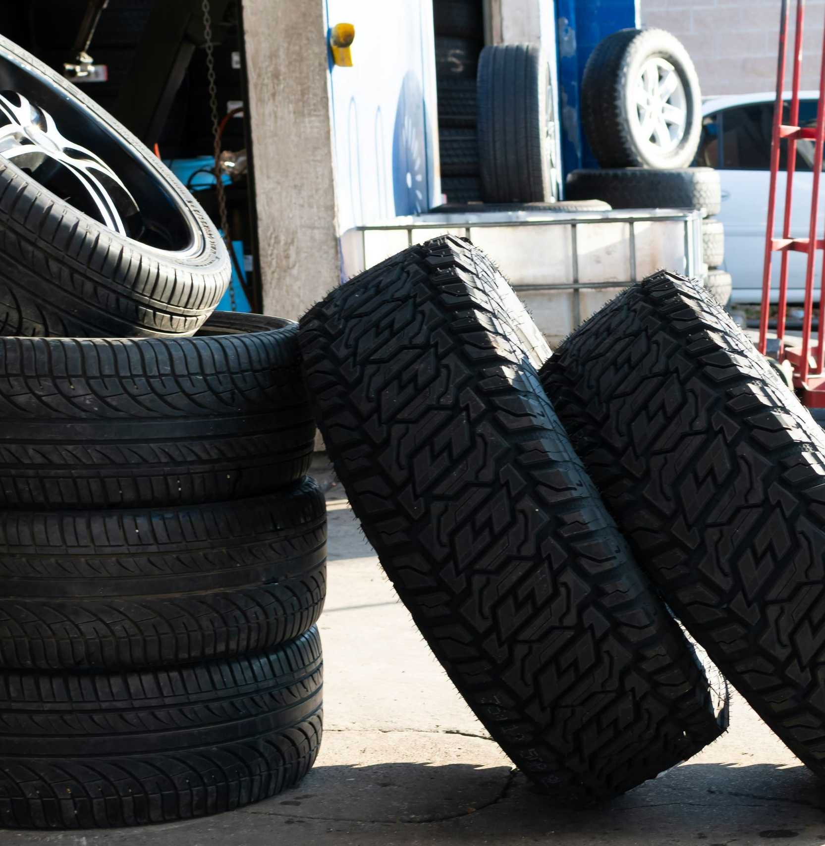 Tires stacked and leaning in a garage setting, sunlight.