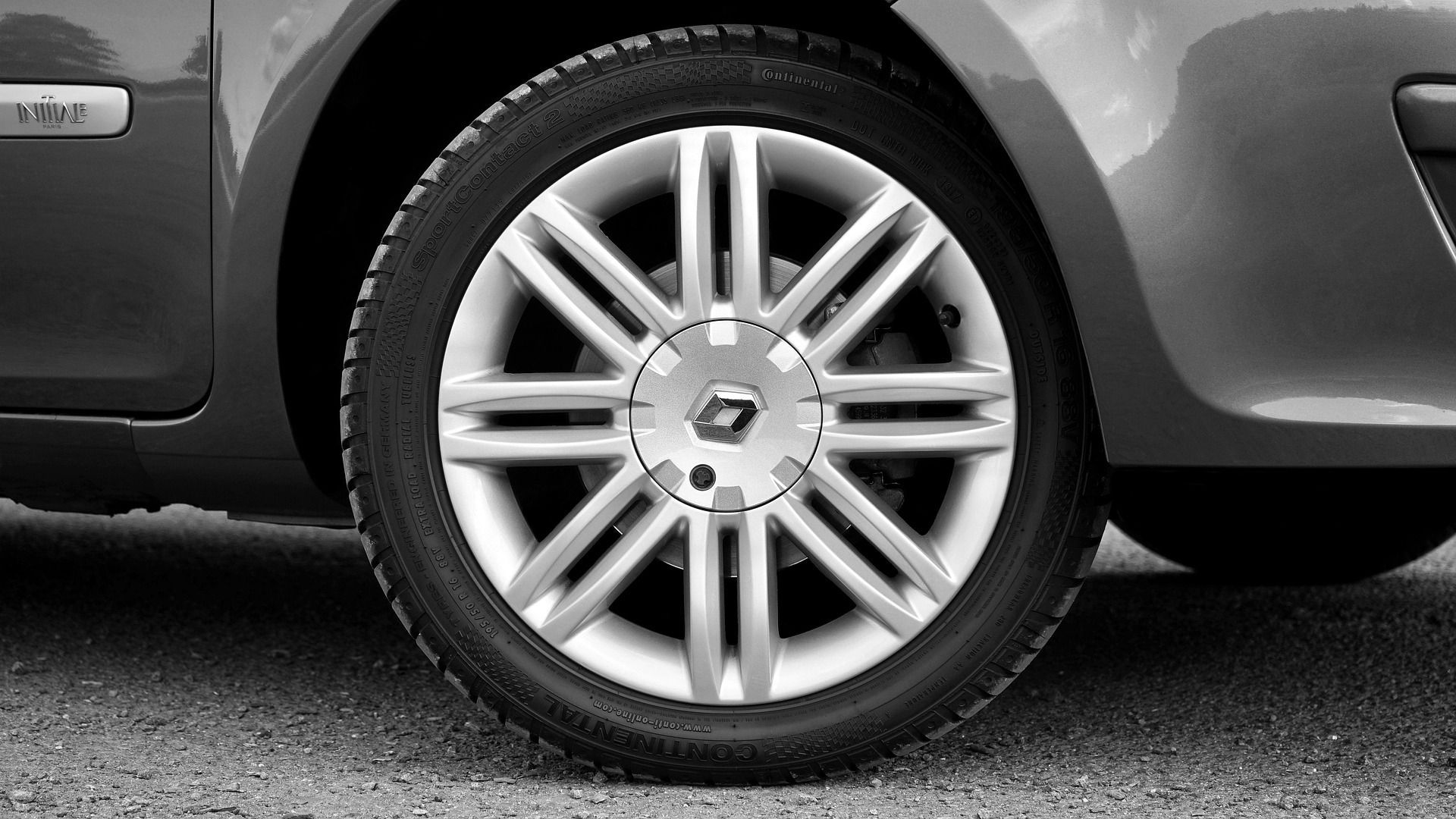 Black and white close-up of a car wheel with a tire and Renault logo, parked on gravel.