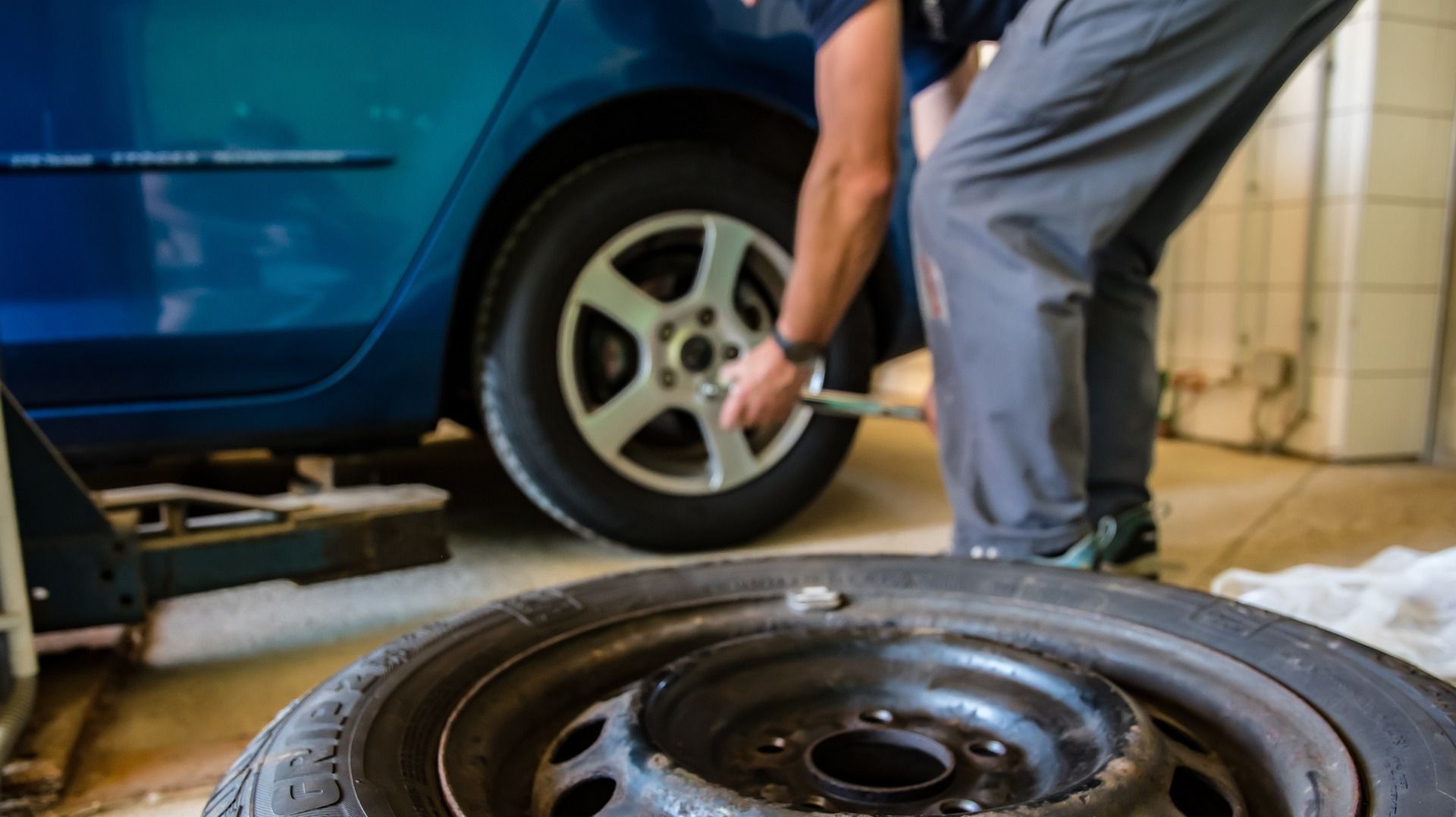 A man is changing a tire on a blue car in a garage.