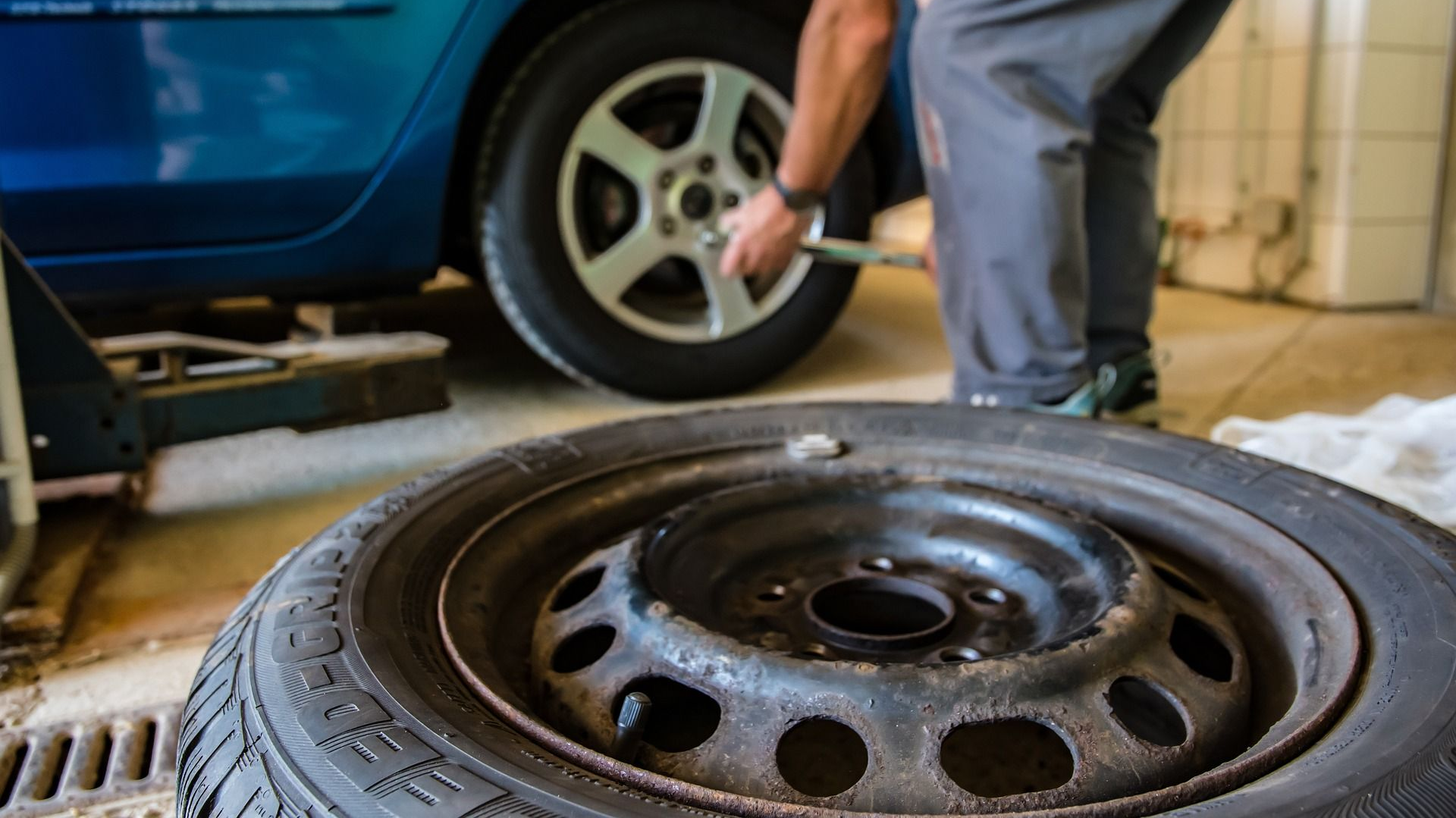 Mechanic changing a car tire in a garage. A blue car is raised, with a spare tire in the foreground.
