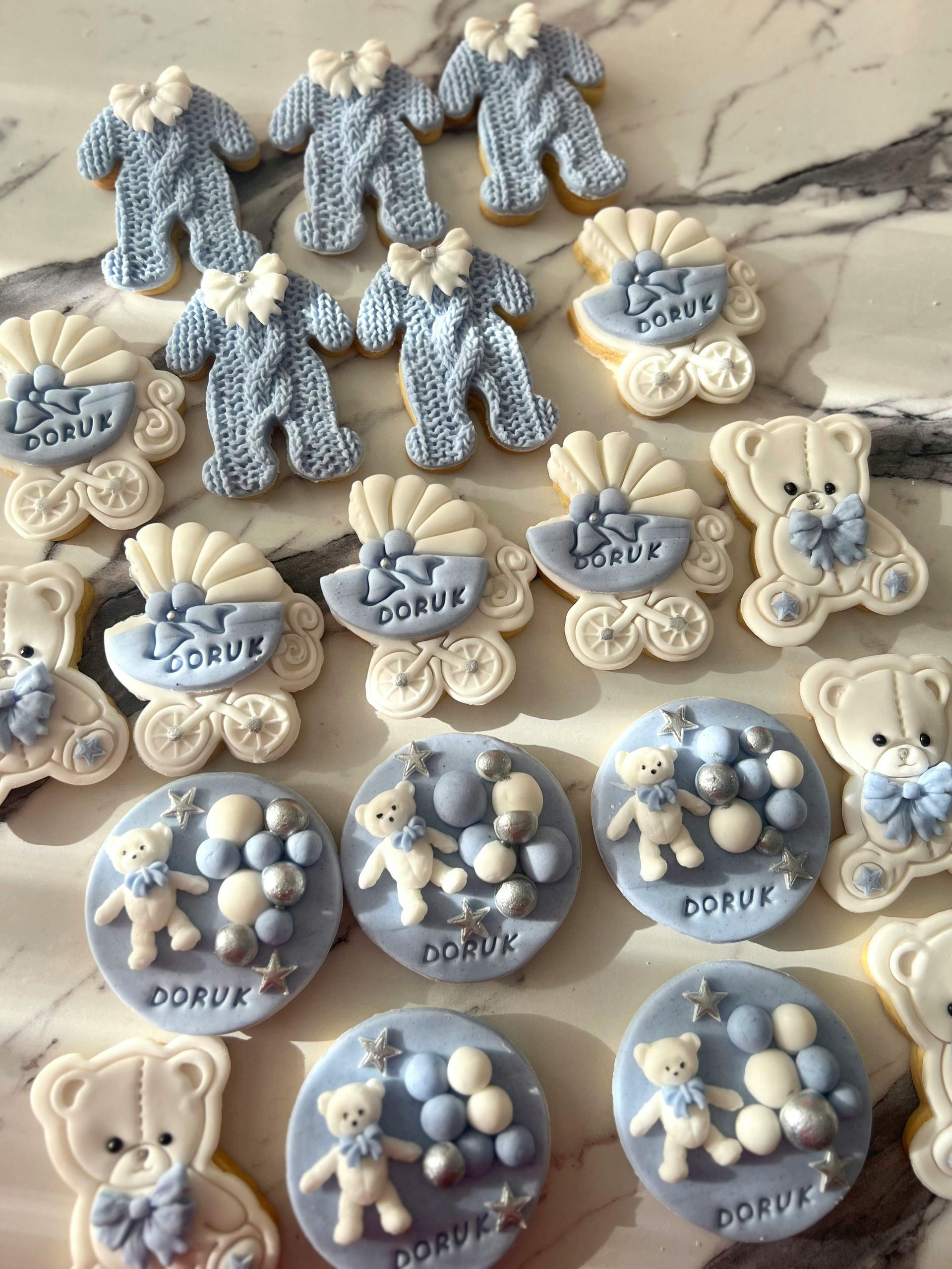 Baby shower cookies with blue and white frosting: onesies, strollers, teddy bears, and circular cookies with 