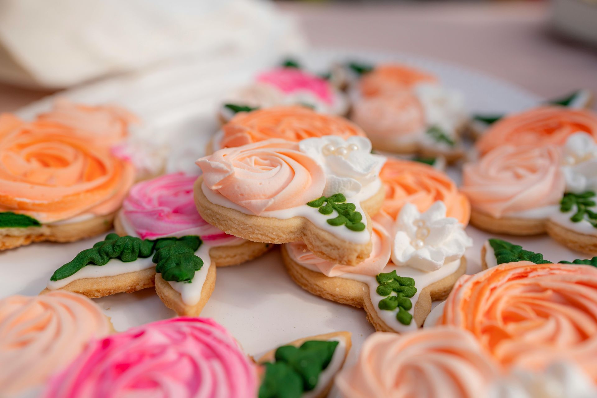 Plate of flower-shaped sugar cookies with orange, pink, and white frosting, and green leaf detail.