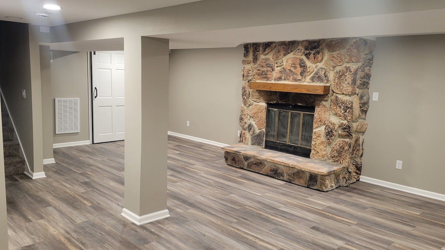 Empty living room with gray wood floors, stone fireplace, and open doorway to a hallway