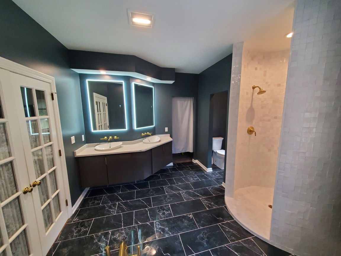 Bathroom with blue-gray walls, curved vanity, lit mirror, glass shower door, and dark tiled floor.