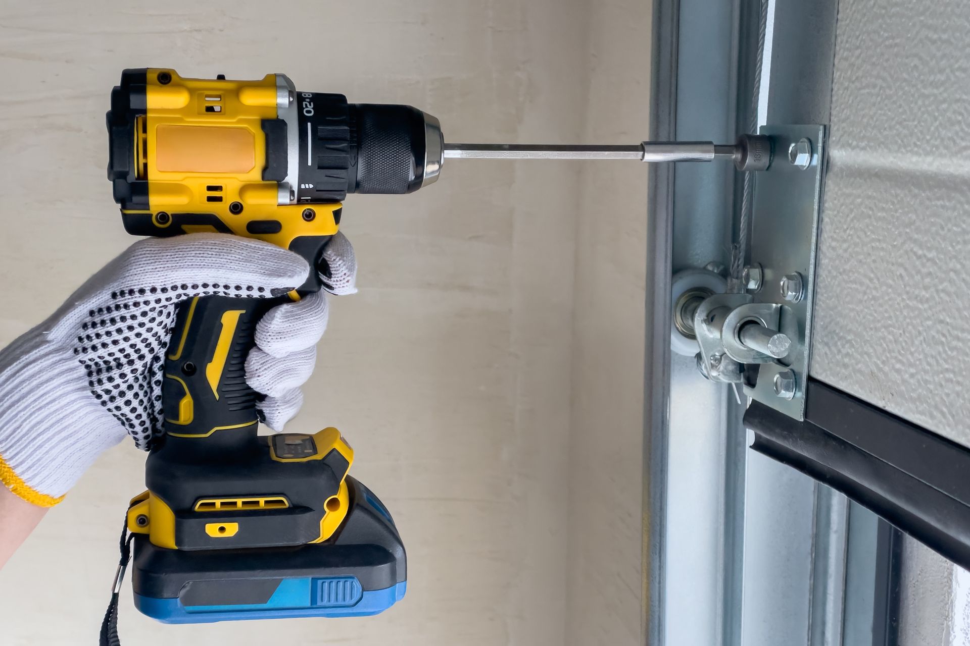 Gloved hand using a cordless drill to tighten hardware on a garage door track. Gloved hand using a cordless drill to tighten hardware on a garage door track.