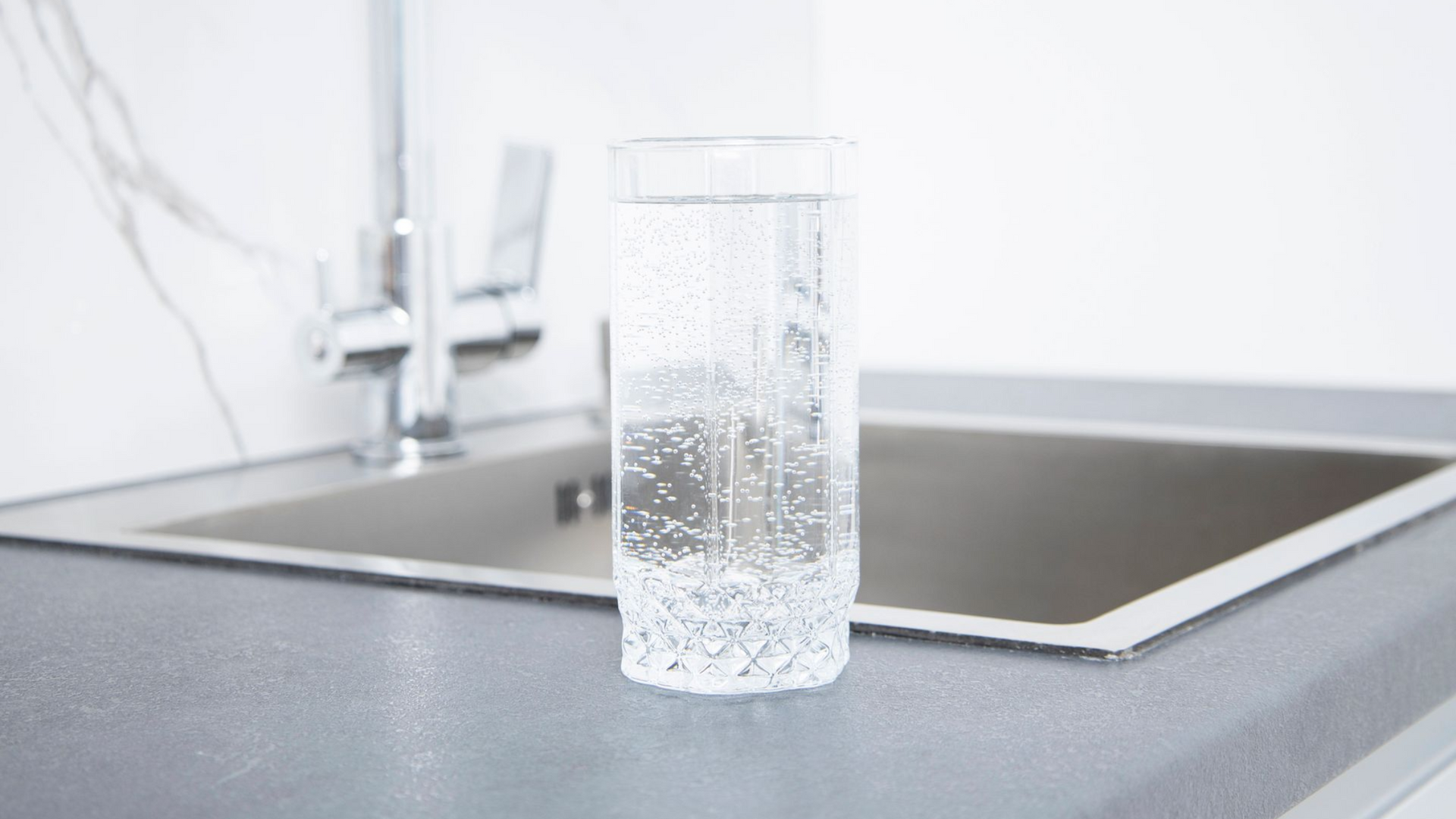 Un bicchiere d'acqua con le bollicine su un piano di lavoro accanto al lavandino.