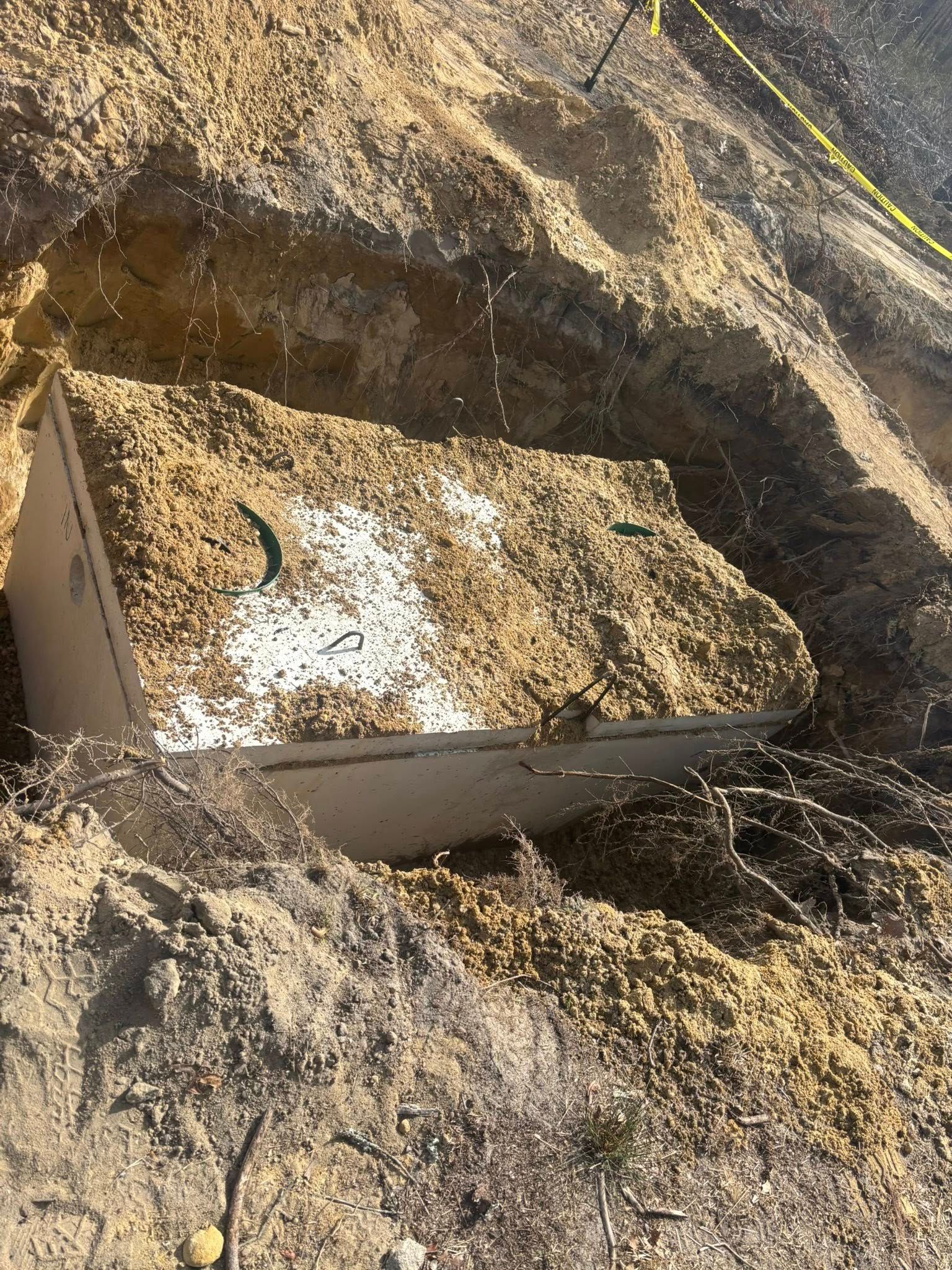 A tilted rectangular box buried in sand and debris.