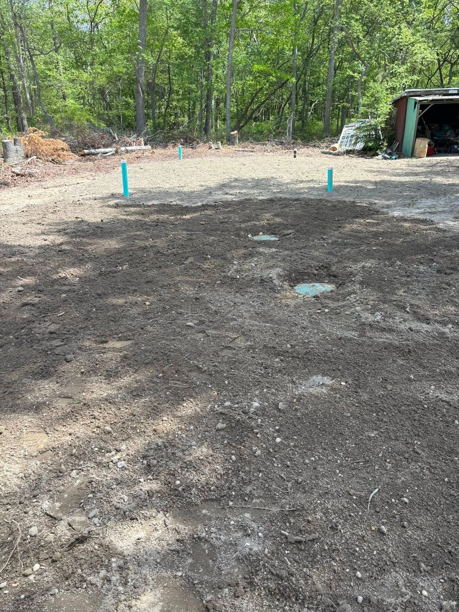 Prepared garden bed with exposed pipes in a clearing near trees and a shed.