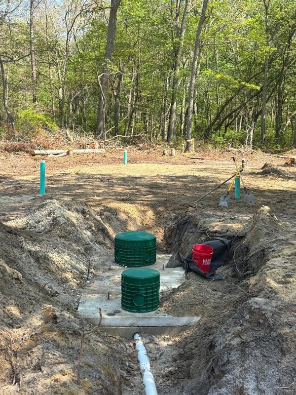 Installation of a septic system in a wooded area. Two green filter covers sit in a concrete base.